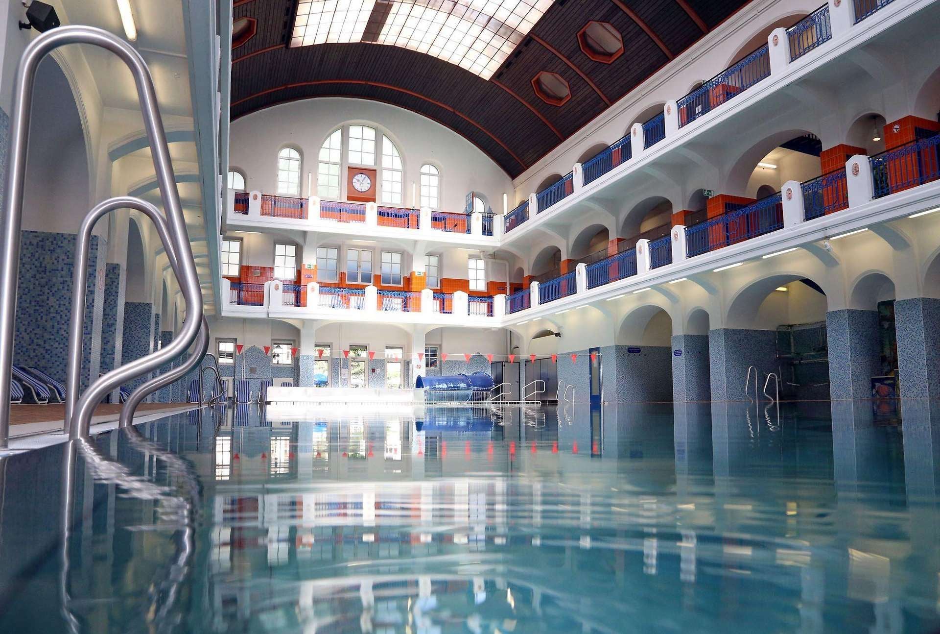 Hallenbad mit historischem Flair, großen Fenstern, blauen Geländern und einem Becken im Jörgerbad.