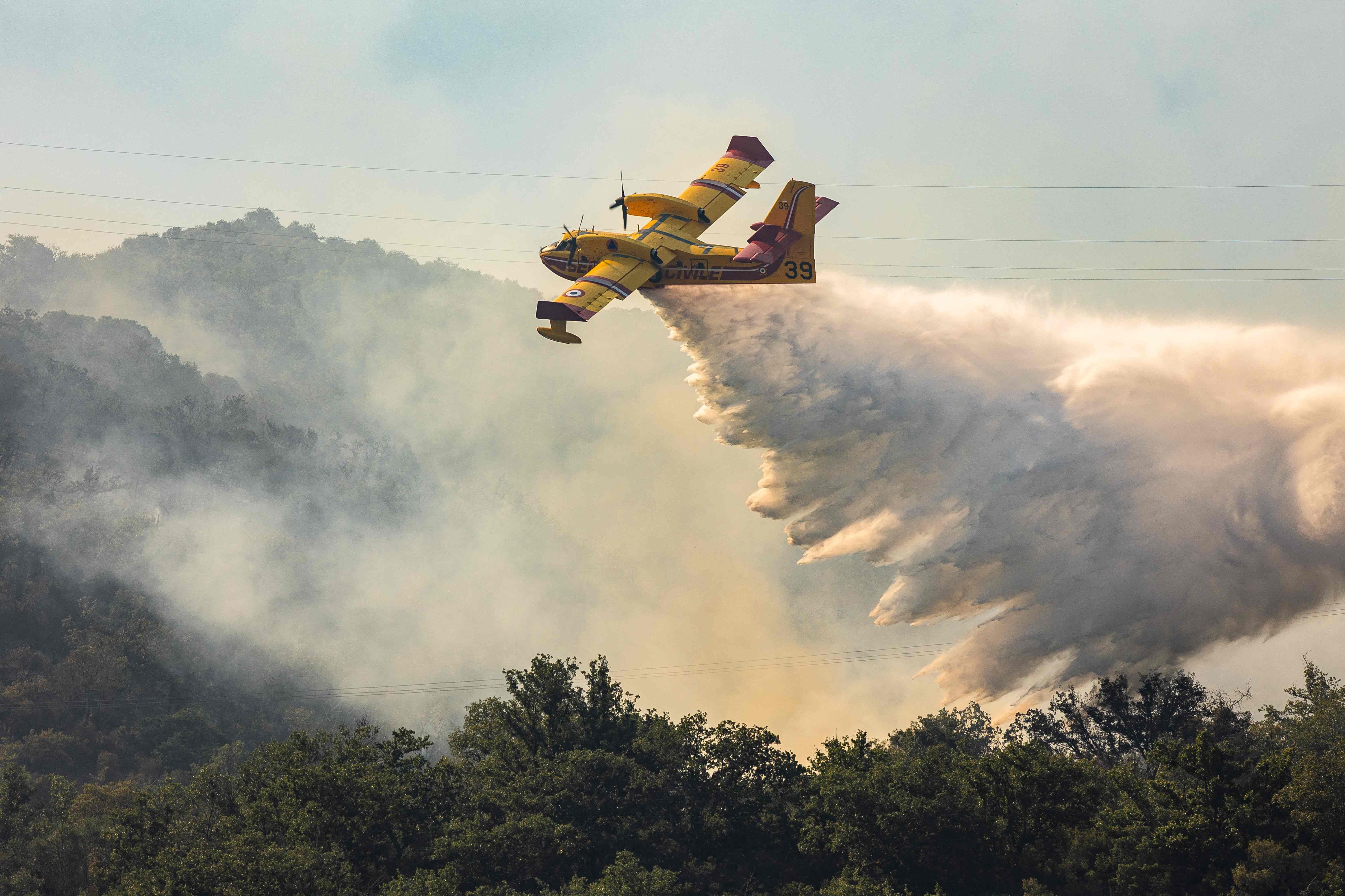 A Canadair CL-415 water bombing aircraft of France's Civil Security services drops water on a wildfire in the southern France departmennt of Pyrenees-Orientales where 700 hundred firefighters backed by special aircraft battled to control a 'gigantic' blaze spreading in a hard-to-reach remote area, with more than 10,000 local residents evacuated, near the town of Bouleternerre on July 6, 2026. Wildfires raged across southern Europe, forcing thousands of people to evacuate their homes and prompting officials to ban spectators from a stage of the storied Tour de France cycling race. (Photo by Jc Milhet / AFP)