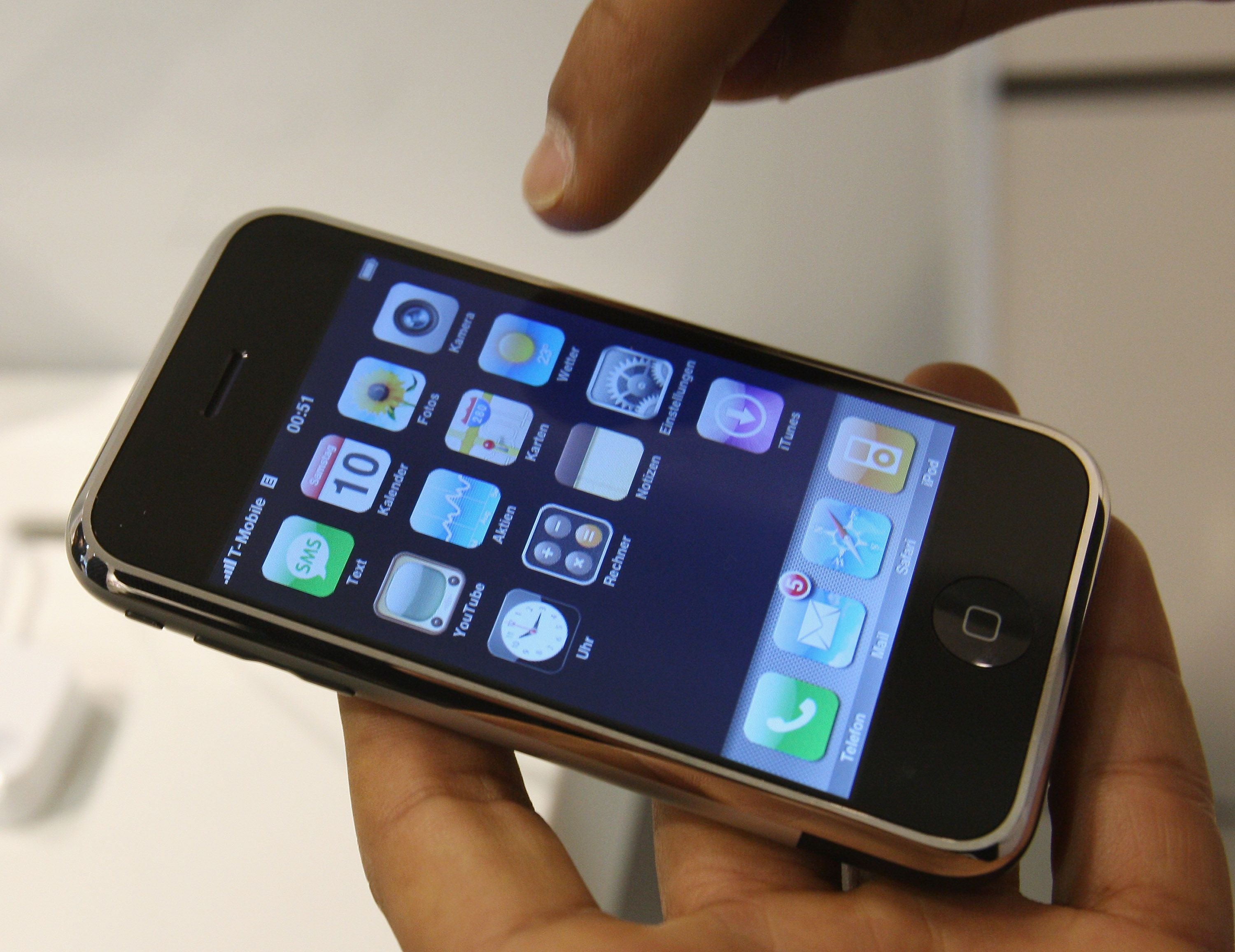 Eine Hand hält ein originales iPhone, das den Startbildschirm mit Apps zeigt.