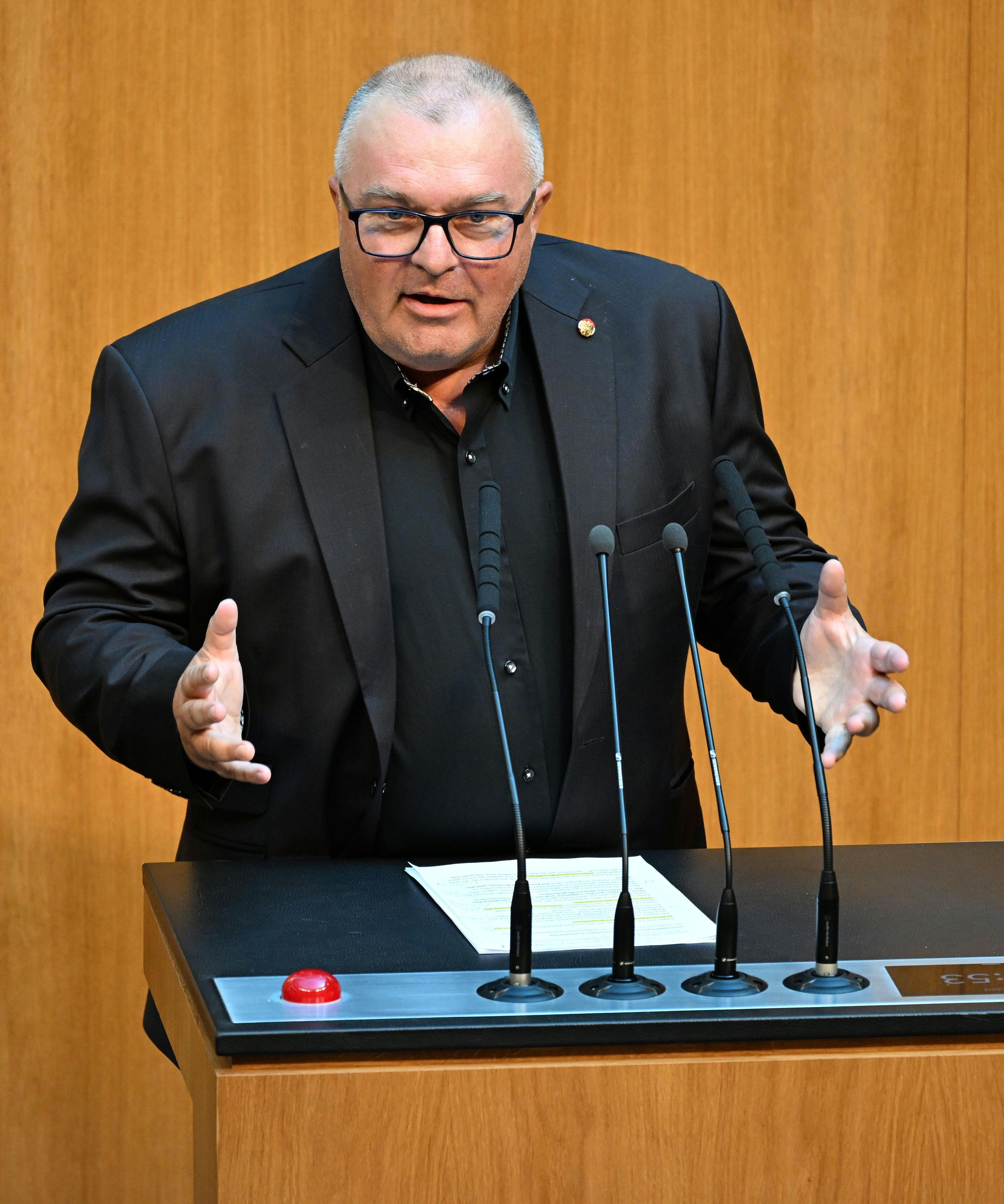 Ein Mann in dunklem Anzug spricht gestikulierend an einem Rednerpult mit mehreren Mikrofonen.