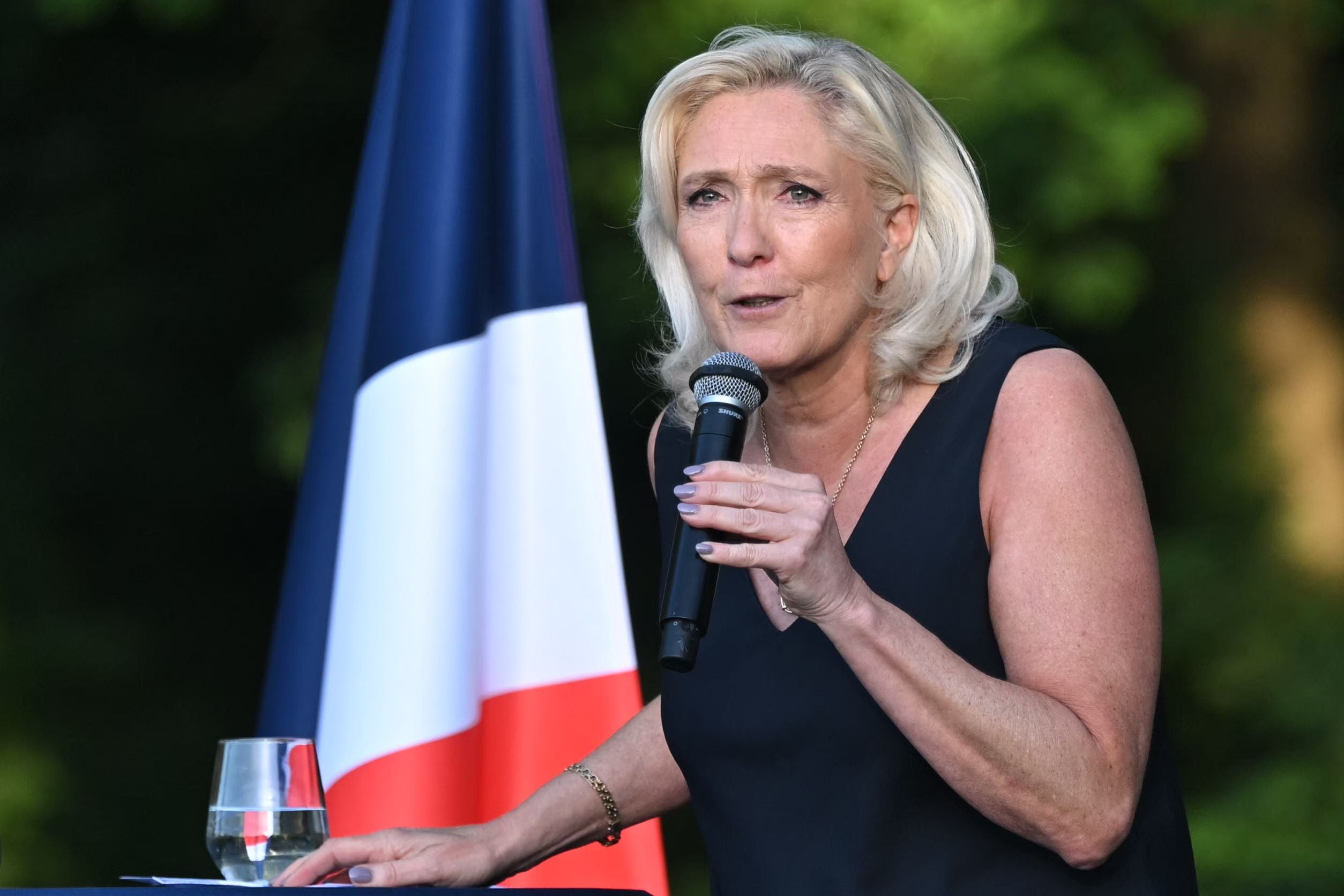 Frau hält eine Rede mit Mikrofon, im Hintergrund eine französische Flagge.