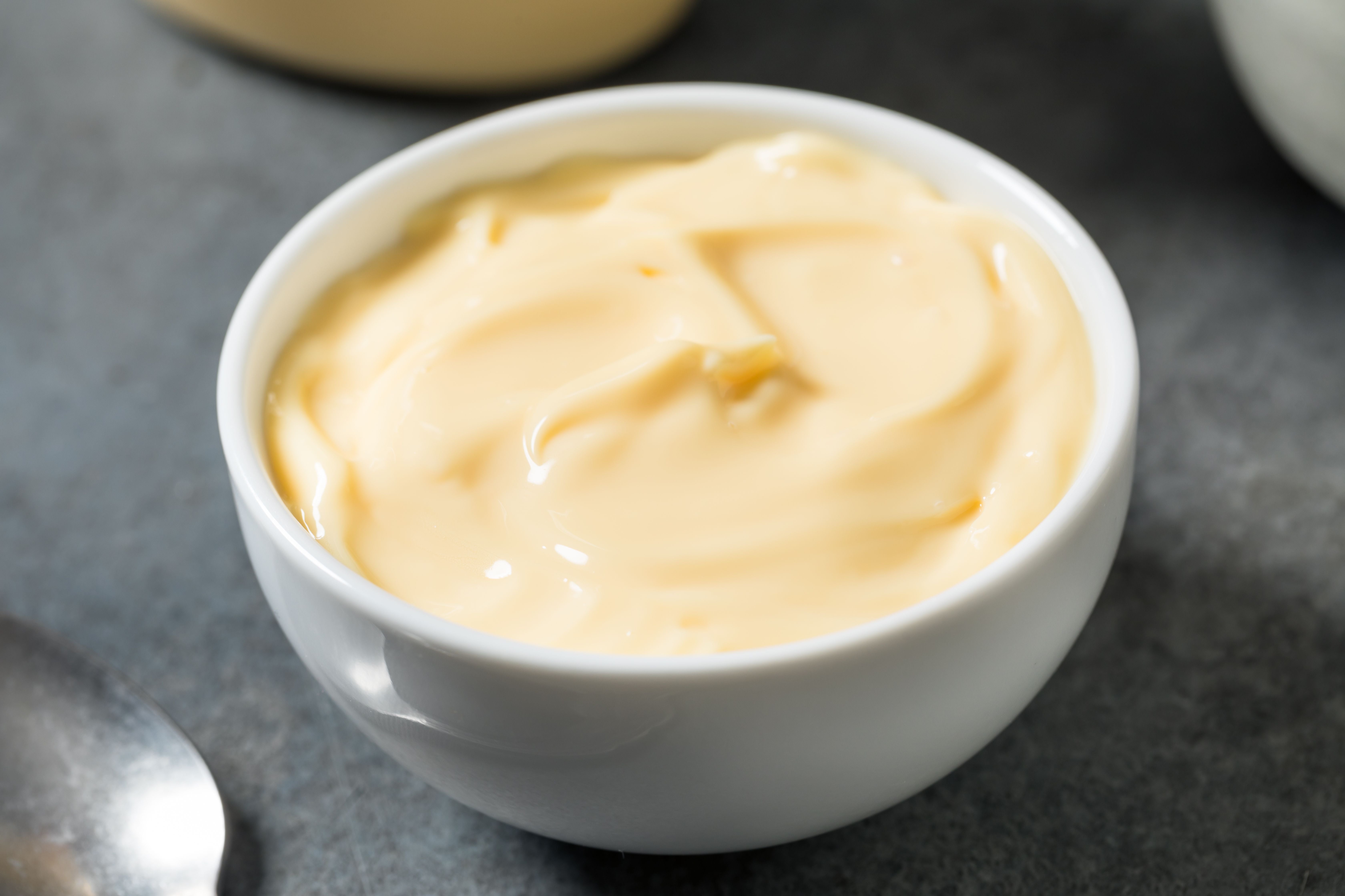 Weiße Schüssel mit cremiger, gelber Mayonnaise auf grauem Untergrund.