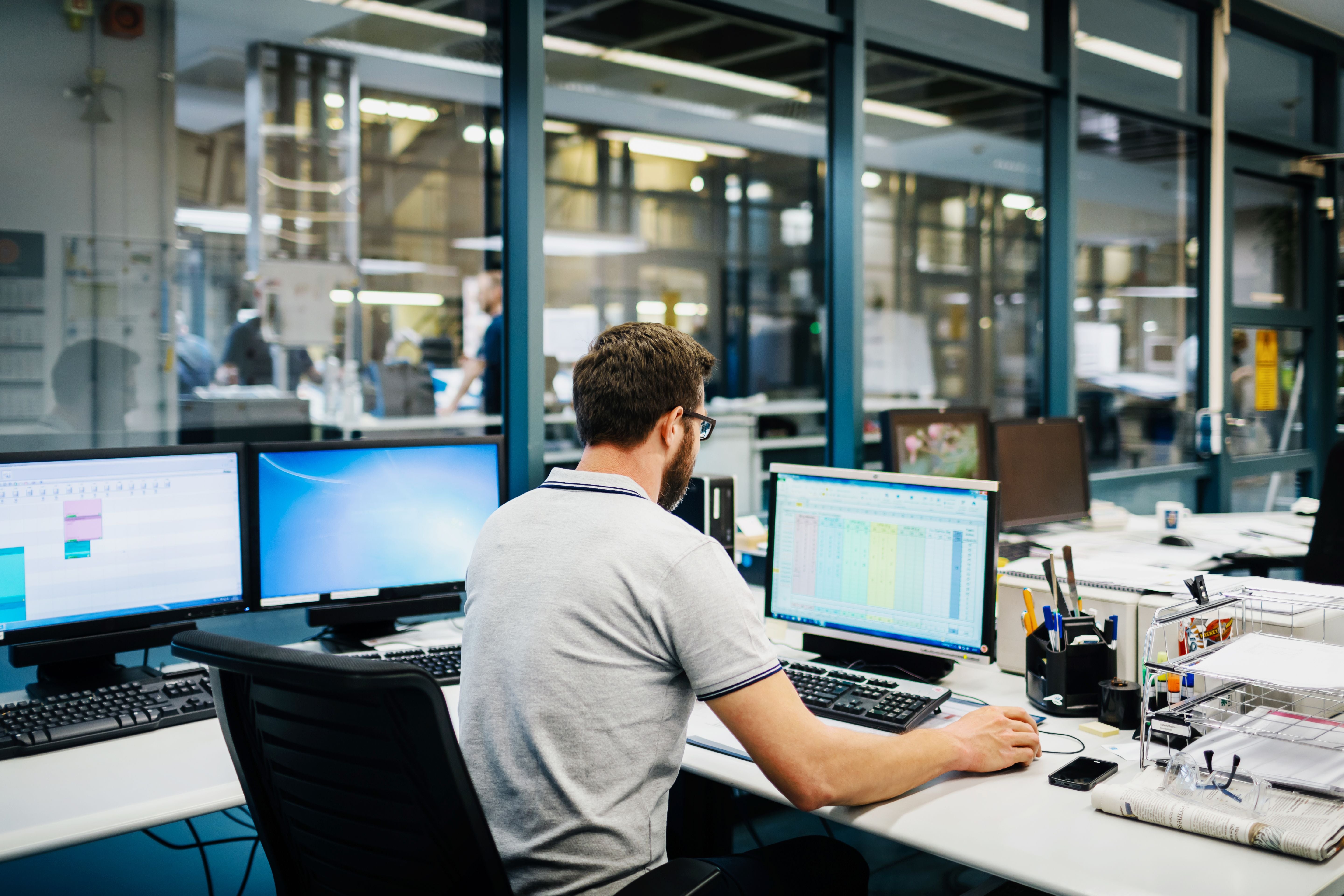 Ingenieur arbeitet in einem Kontrollraum einer Fabrik an mehreren Computern mit Tabellen.