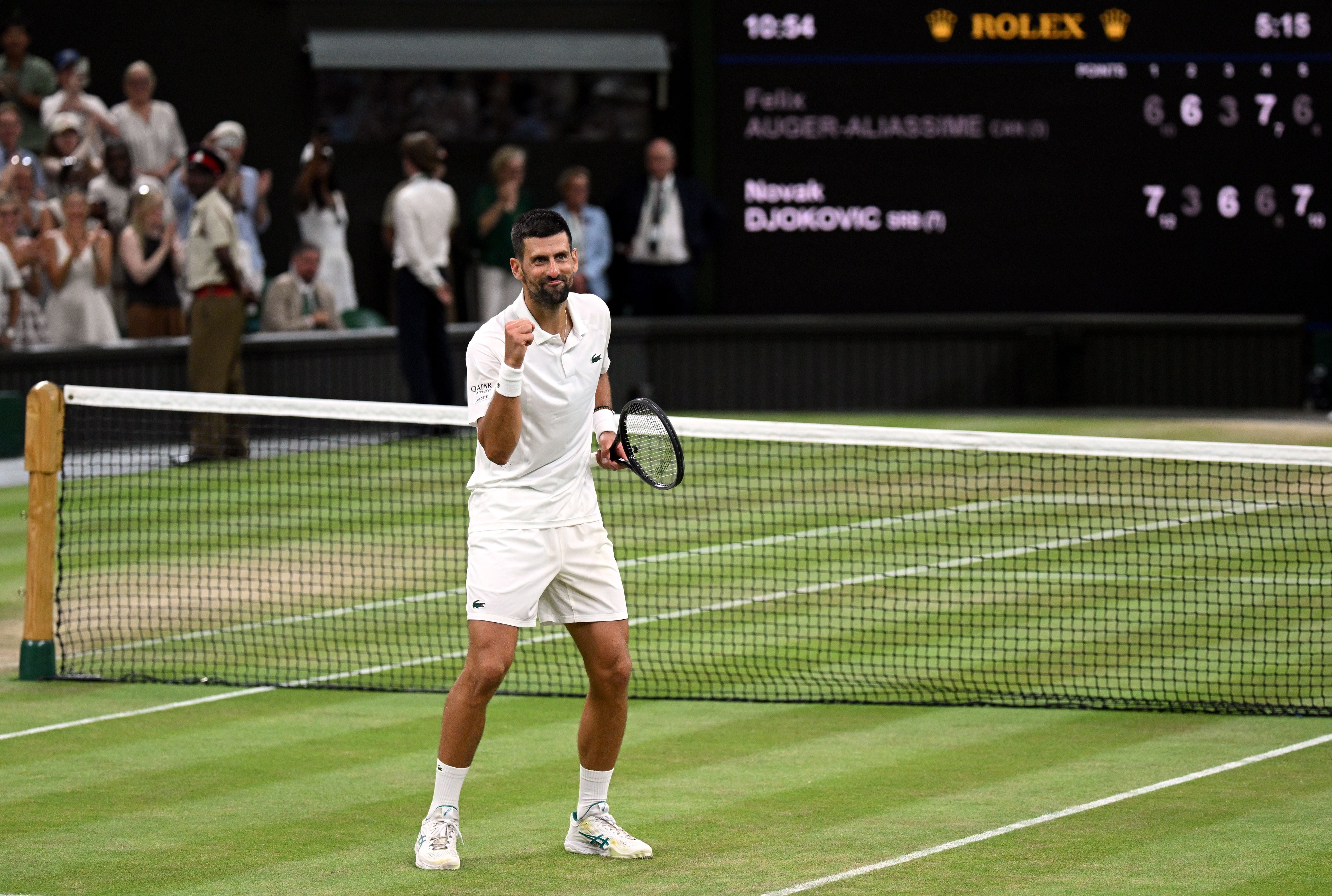 Tennisspieler jubelt auf Rasenplatz, Zuschauer klatschen im Hintergrund, Spielstand ist sichtbar.