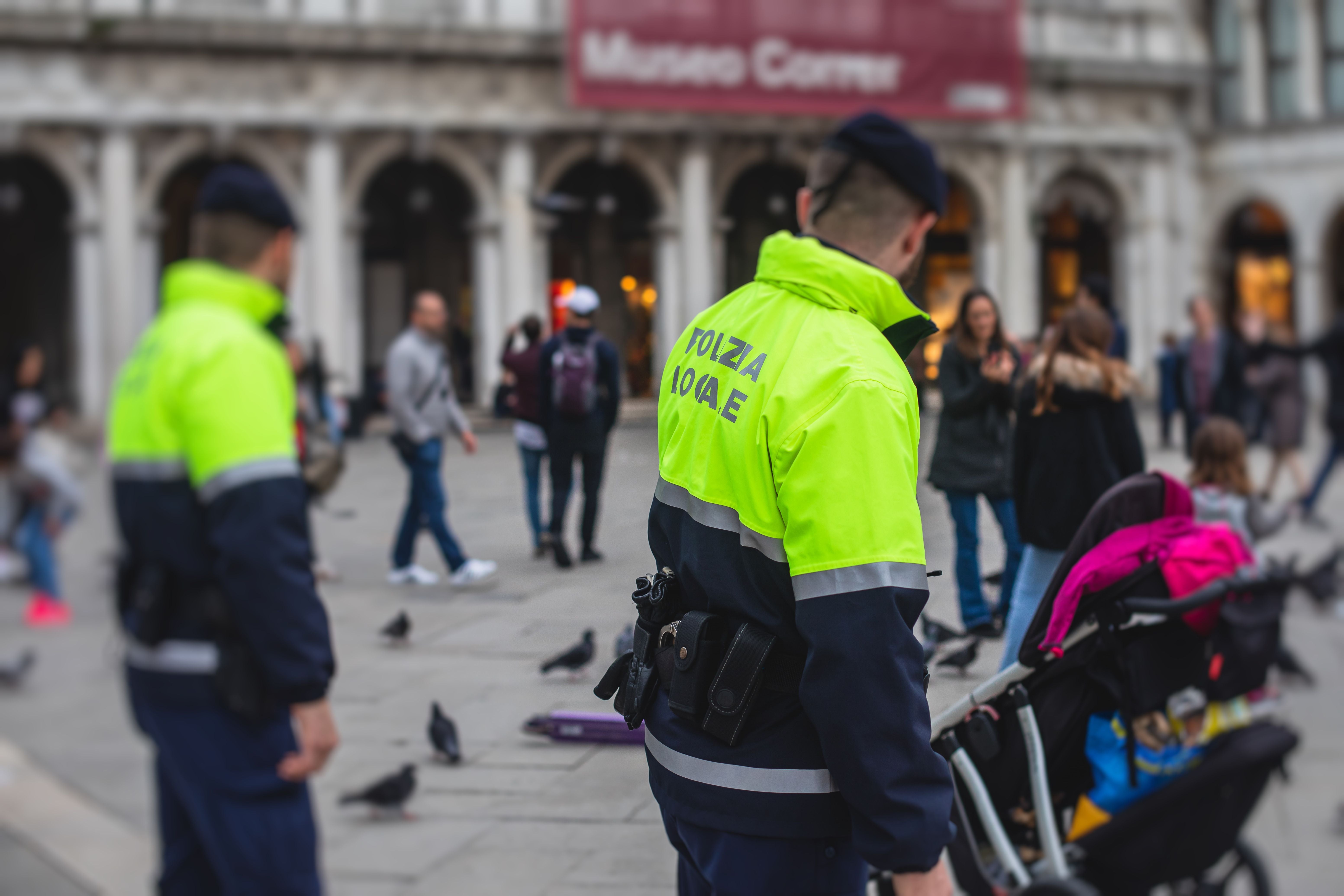 Zwei Polizisten der örtlichen Polizei in Venedig überwachen eine belebte Straße mit Passanten.