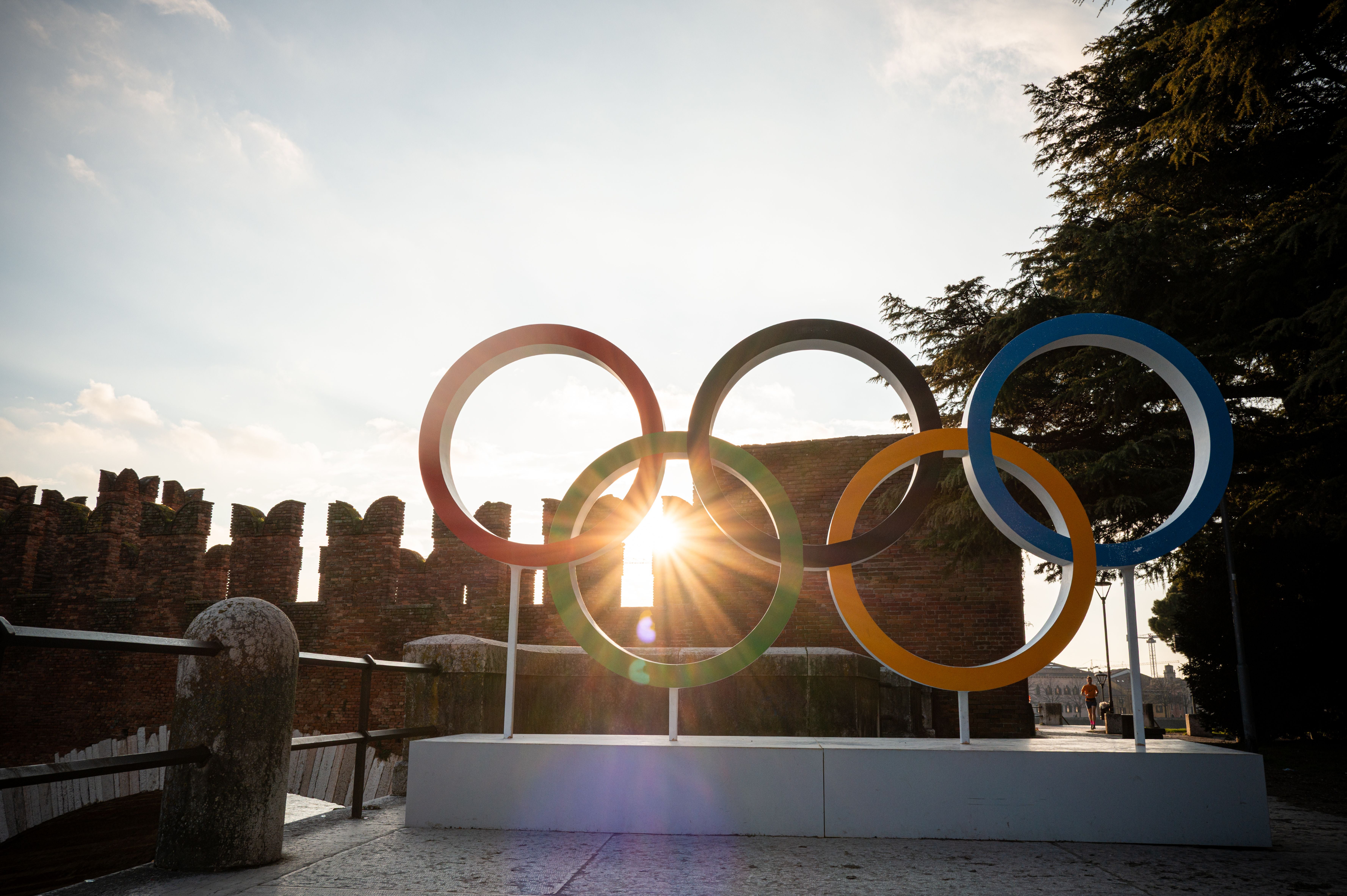 Olympische Ringe vor der Ponte di Castelvecchio in Verona mit Sonnenlicht im Hintergrund.