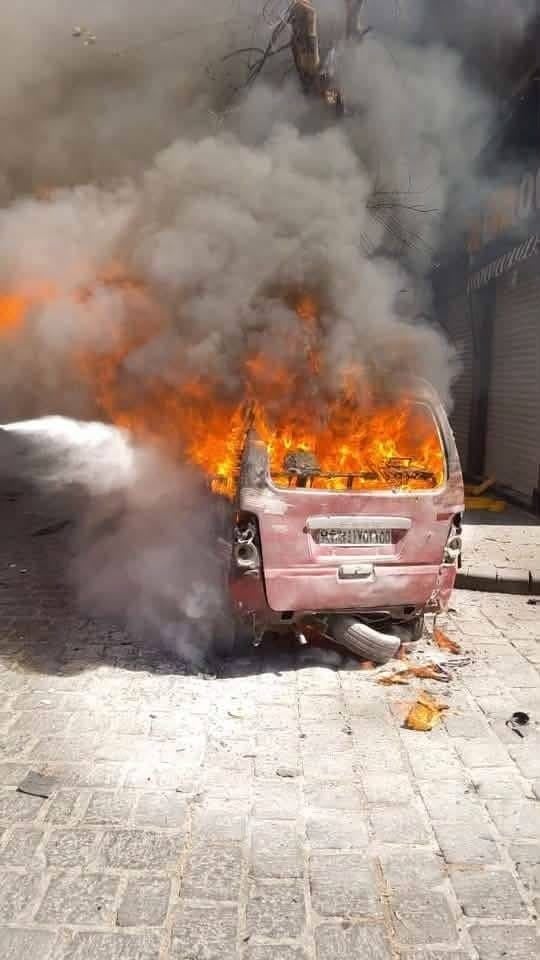 Ein brennendes Auto mit starker Rauchentwicklung auf einer gepflasterten Straße in Damaskus.