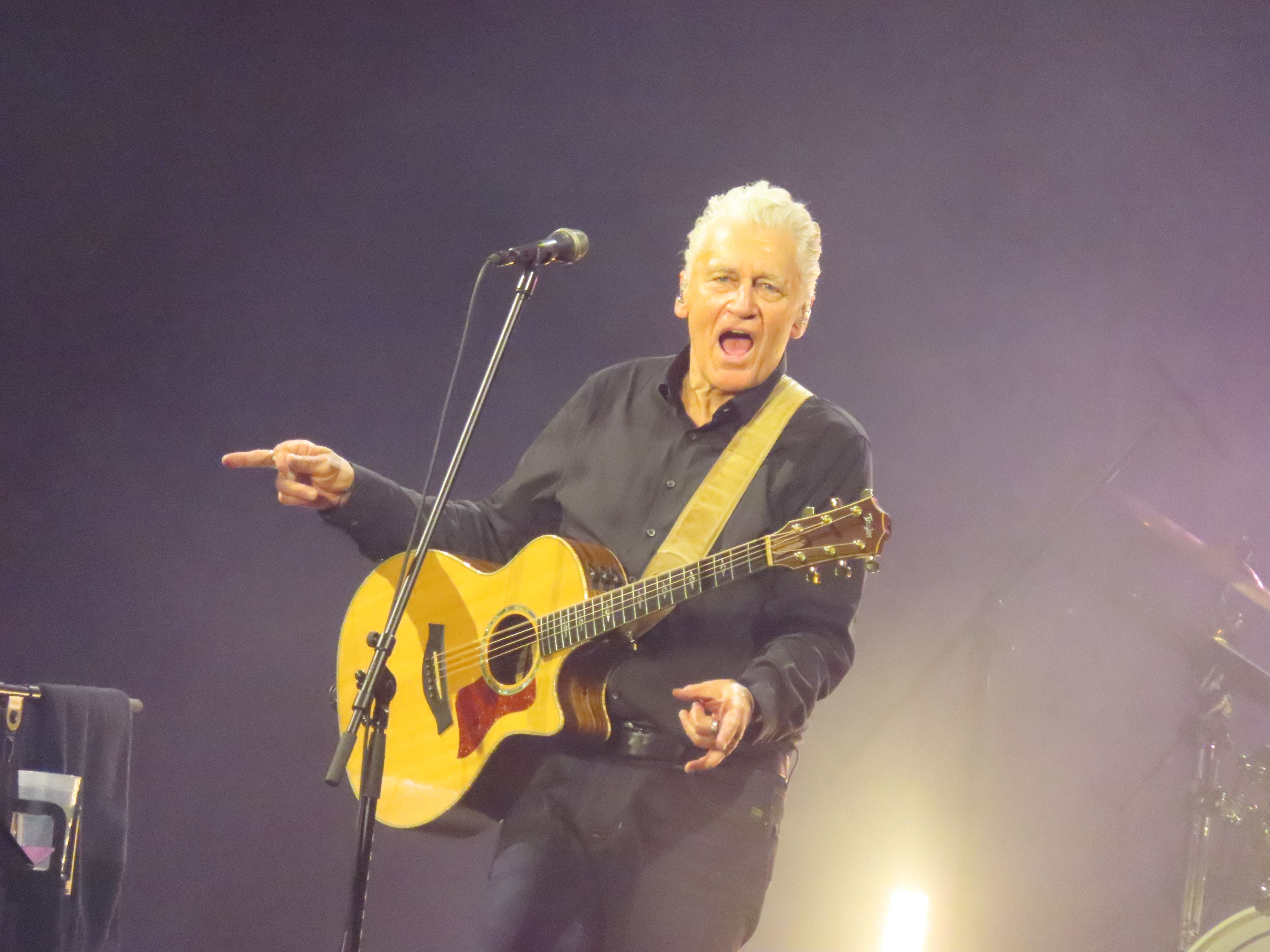 Älterer Mann spielt akustische Gitarre auf der Bühne und zeigt in das Publikum.