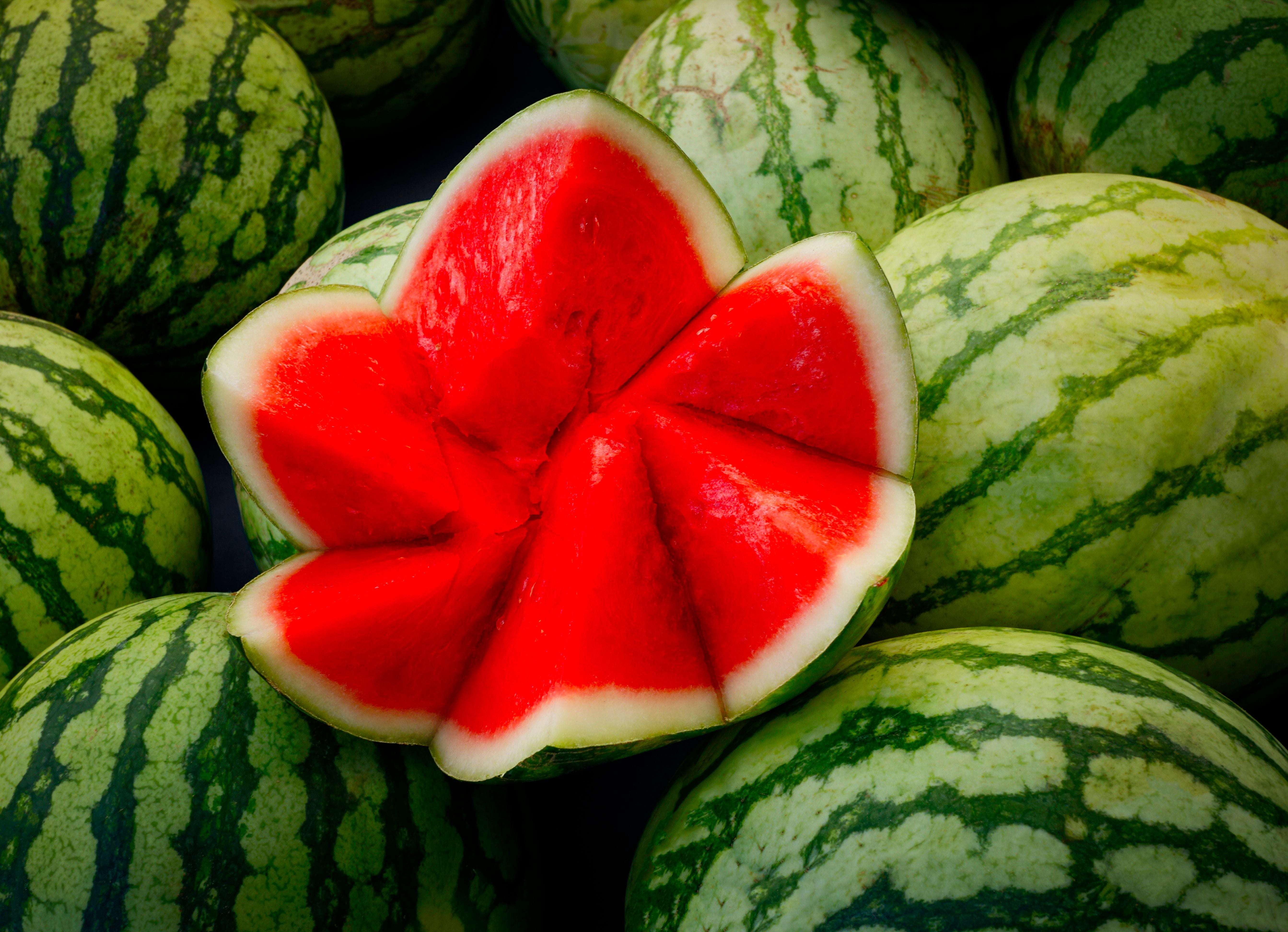 Aufgeschnittene Wassermelone mit rotem Fruchtfleisch liegt auf ganzen Wassermelonen.
