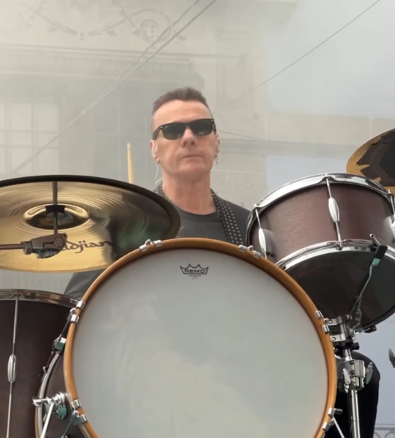 Ein Mann mit Sonnenbrille spielt Schlagzeug bei einer Outdoor-Performance.