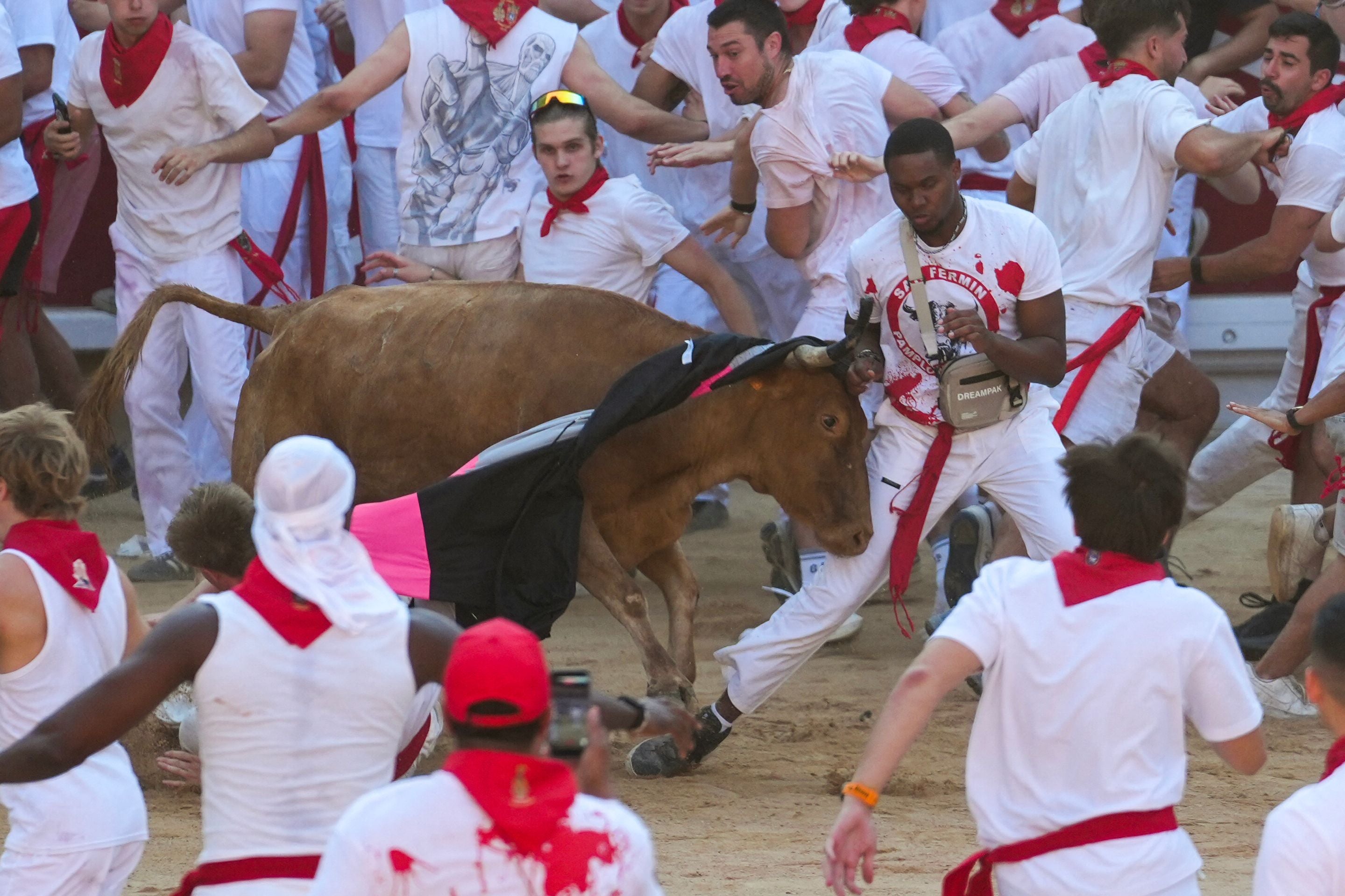Eine junge Kuh rammt einen Läufer, während Menschen beim Stierlauf in Pamplona ausweichen.
