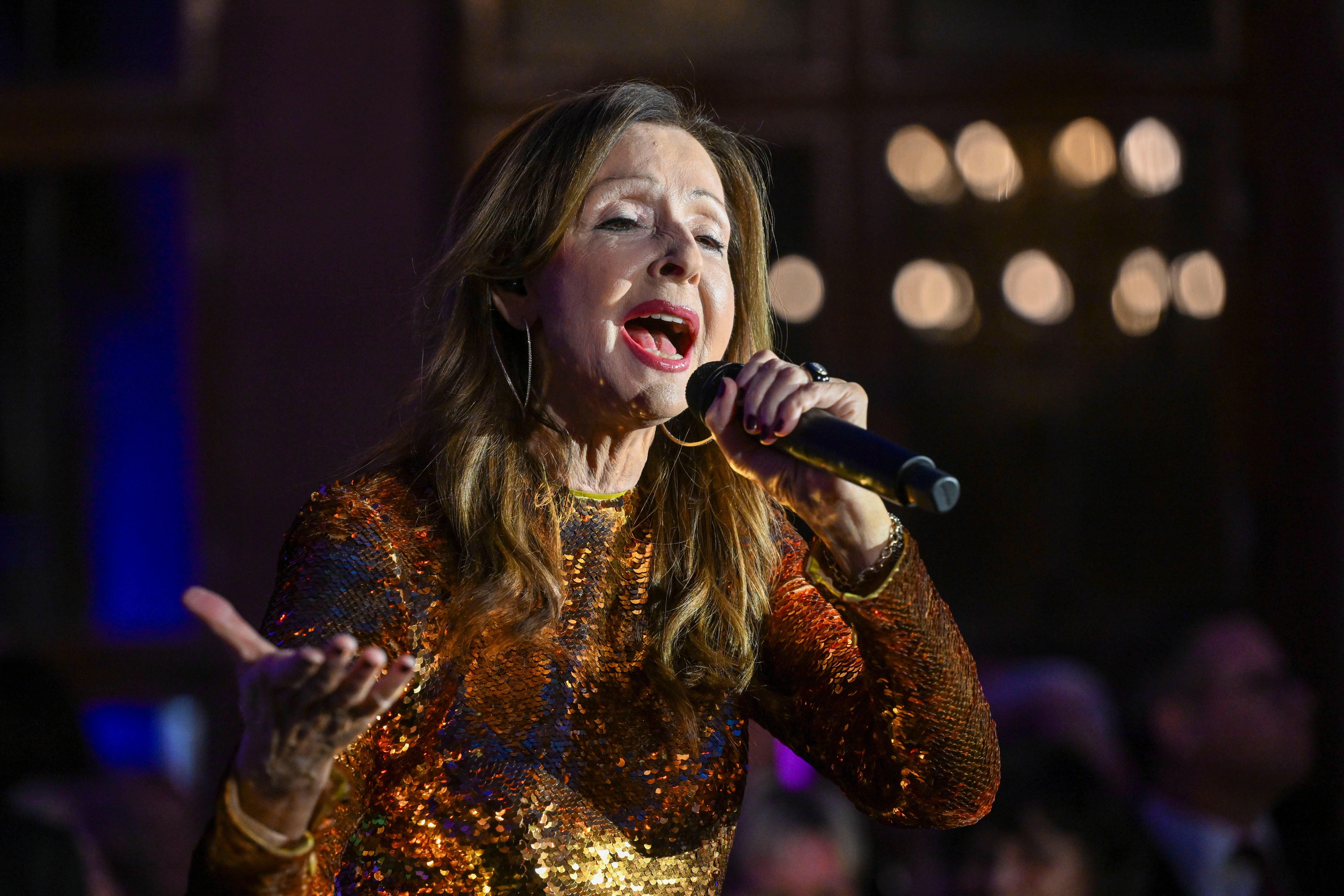 Eine Frau im glitzernden Kleid singt mit Mikrofon auf einer Bühne.