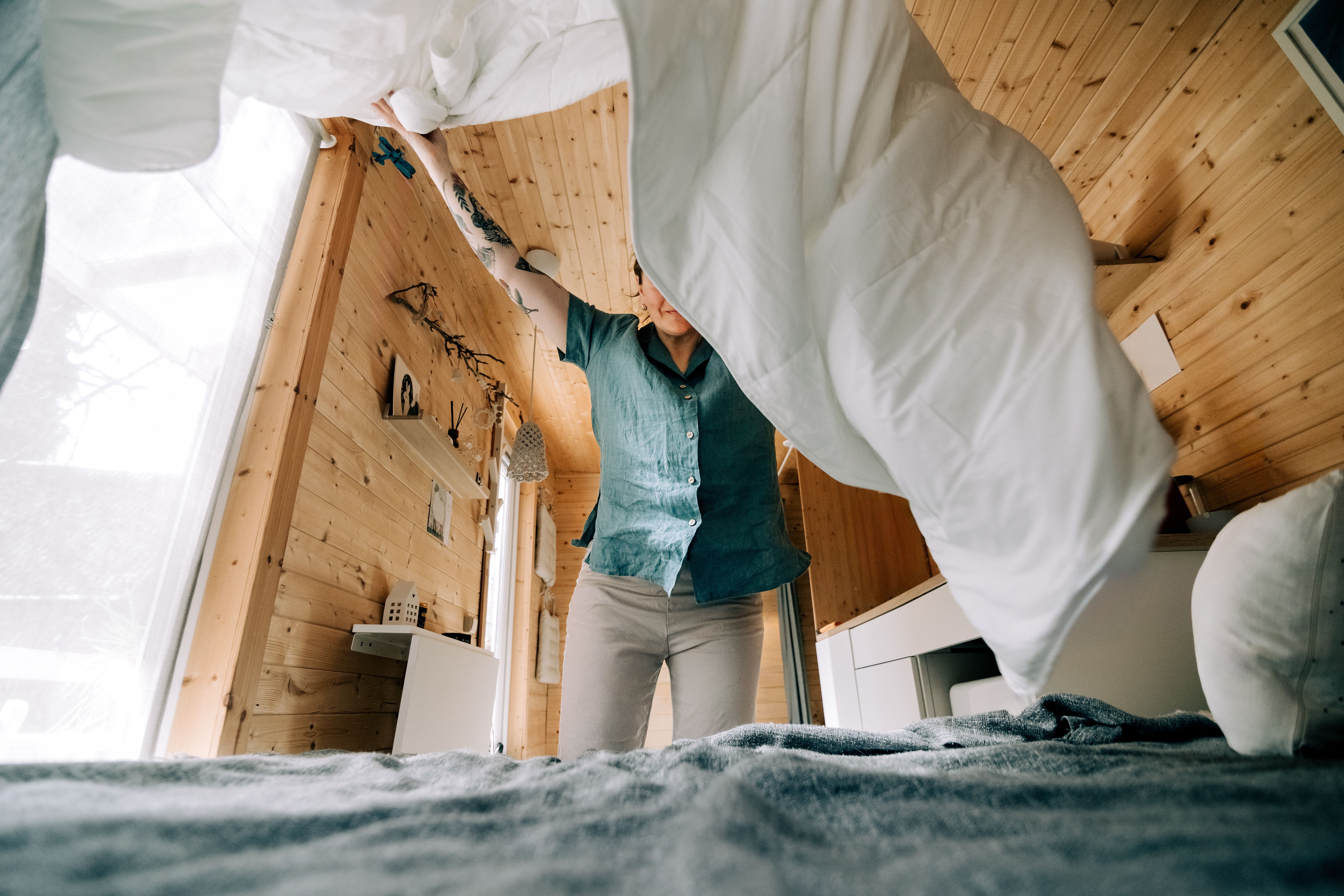 Frau macht das Bett in einem gemütlichen, kleinen Holzhaus.