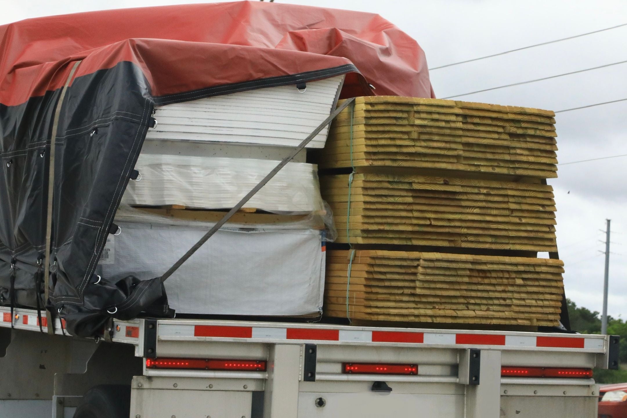 Lastwagen mit gestapelten Steinplatten und Holz, teils mit Plane abgedeckt.