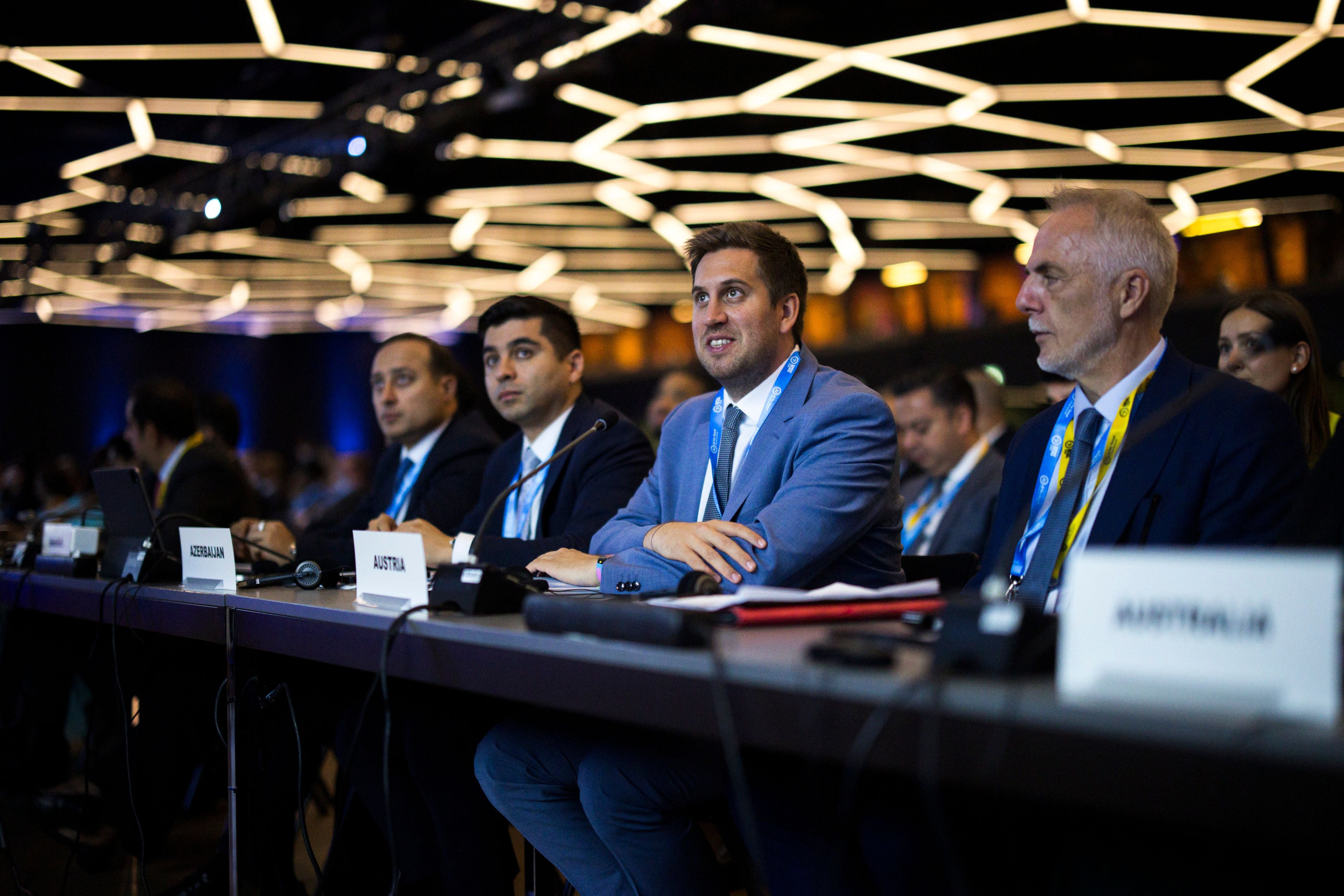 Männer im Anzug sitzen bei einer KI-Konferenz in Genf an einem Konferenztisch.