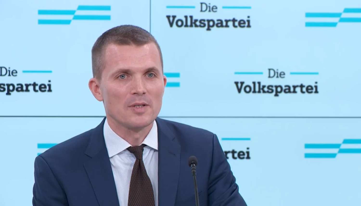 Ein Mann im Anzug spricht bei einer Pressekonferenz vor „Die Volkspartei“-Logos.