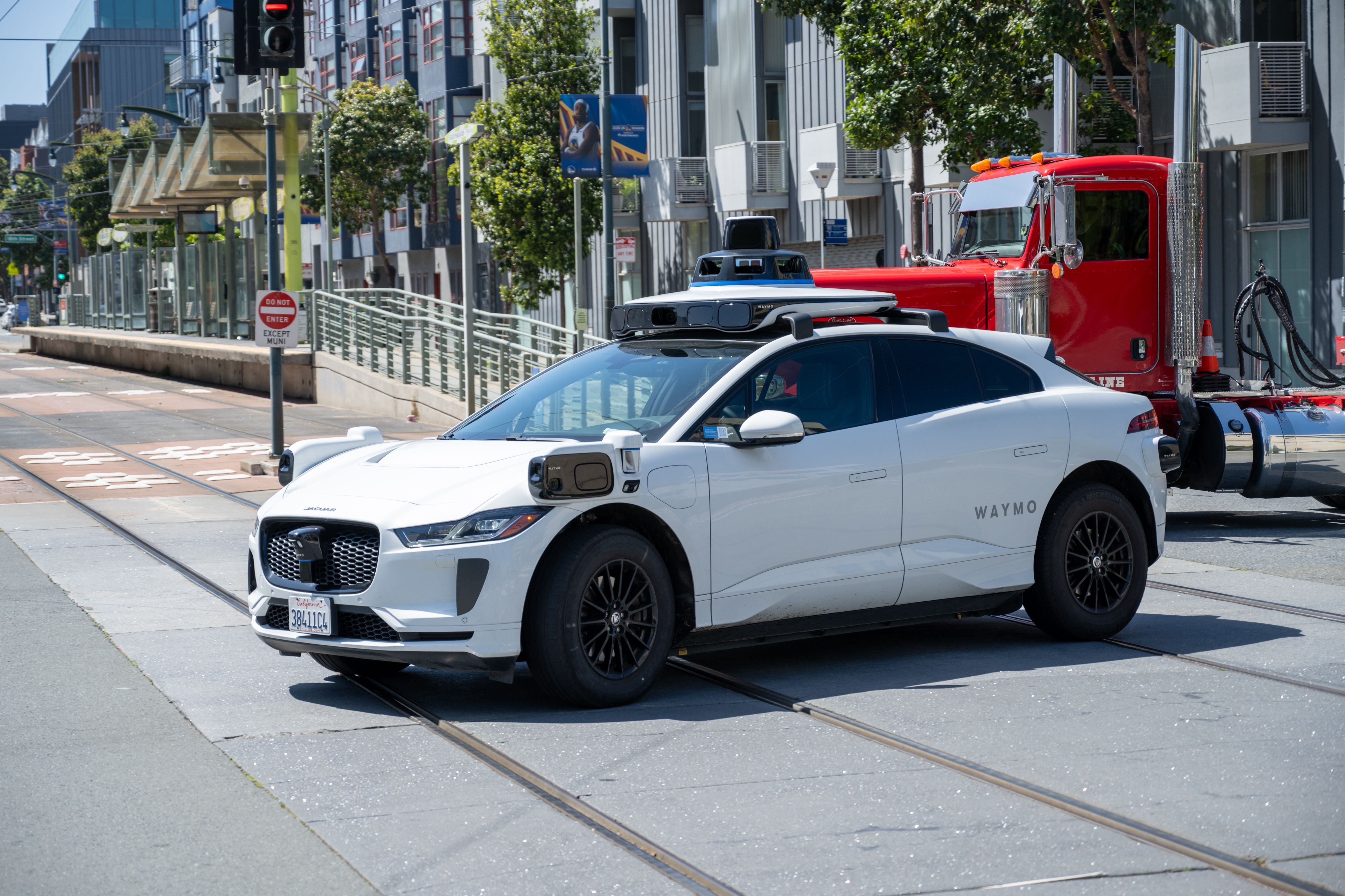 Autonomes Waymo Jaguar I-PACE Testfahrzeug überquert Straßenbahngleise in San Francisco bei Sonnenschein.