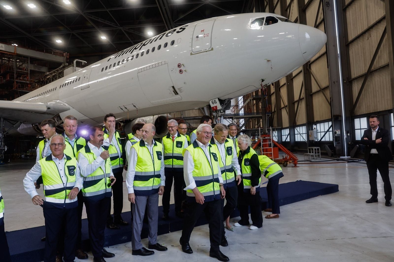 Gruppe von Menschen in Warnwesten steht vor einem Flugzeug in einer Flugzeughalle.