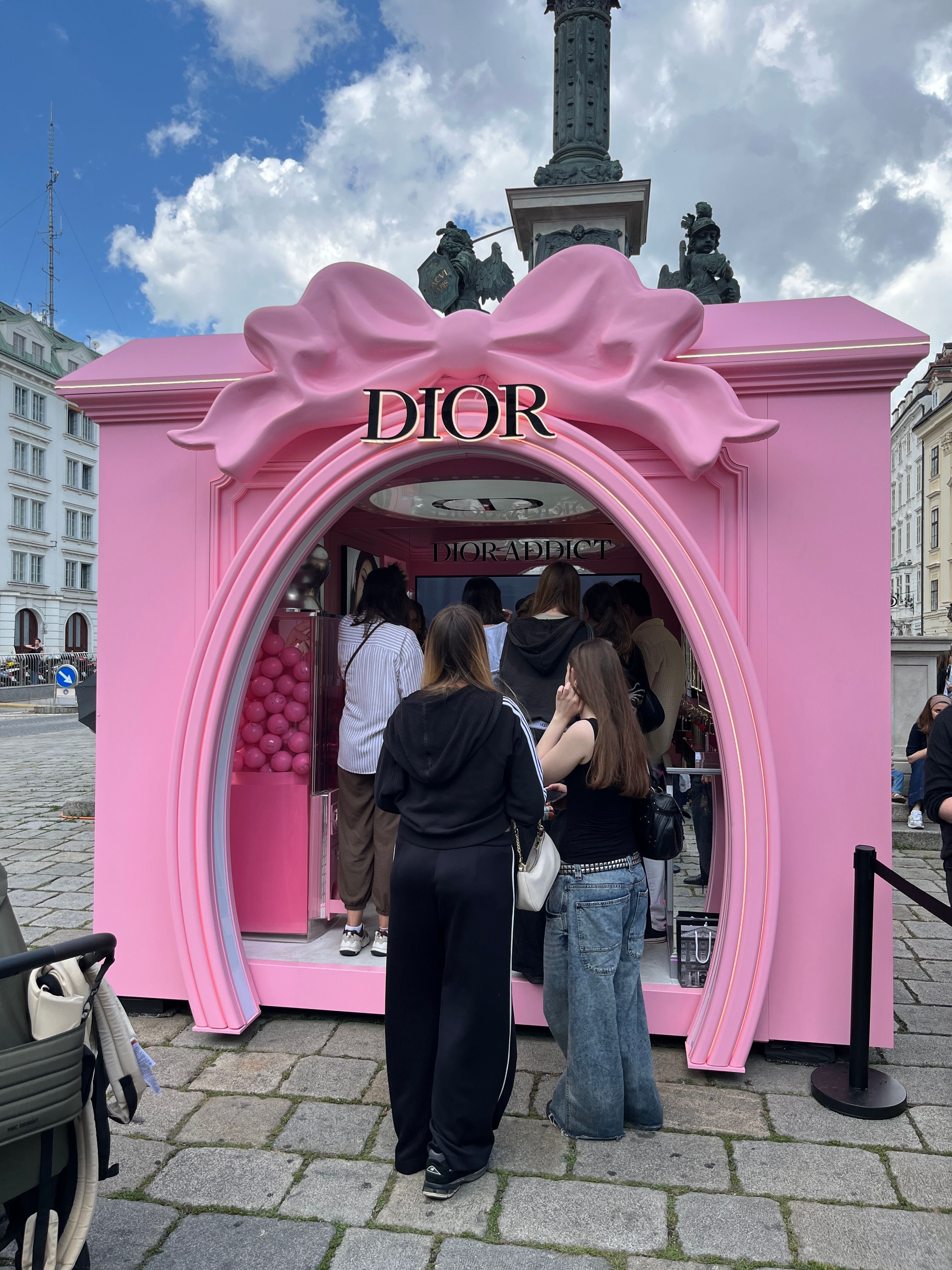Mehrere Menschen stehen vor einem rosafarbenen Dior-Pop-up-Stand mit großer Schleife.
