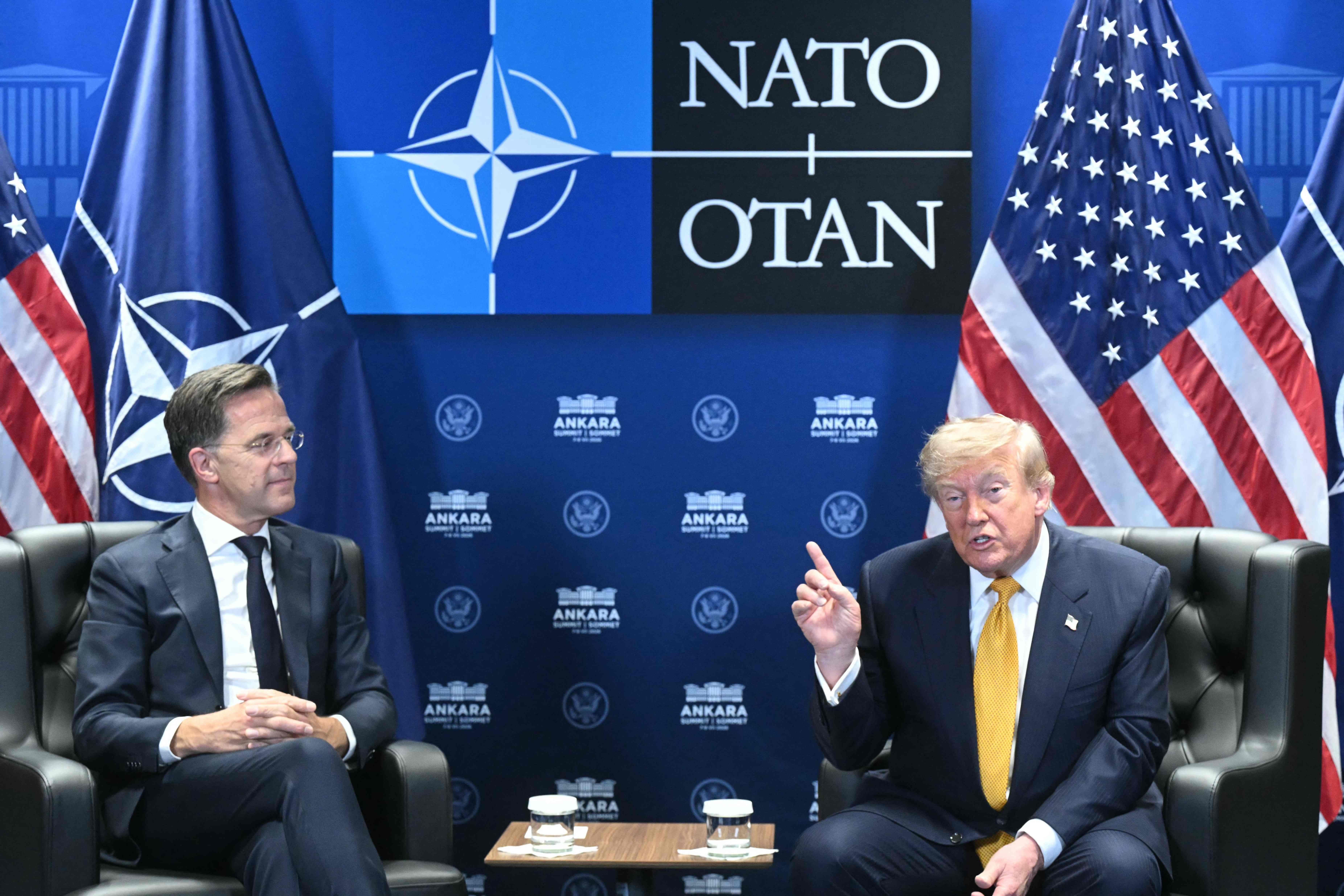 Zwei Männer sitzen vor NATO- und US-Flaggen auf Sesseln beim NATO-Gipfel in Ankara.