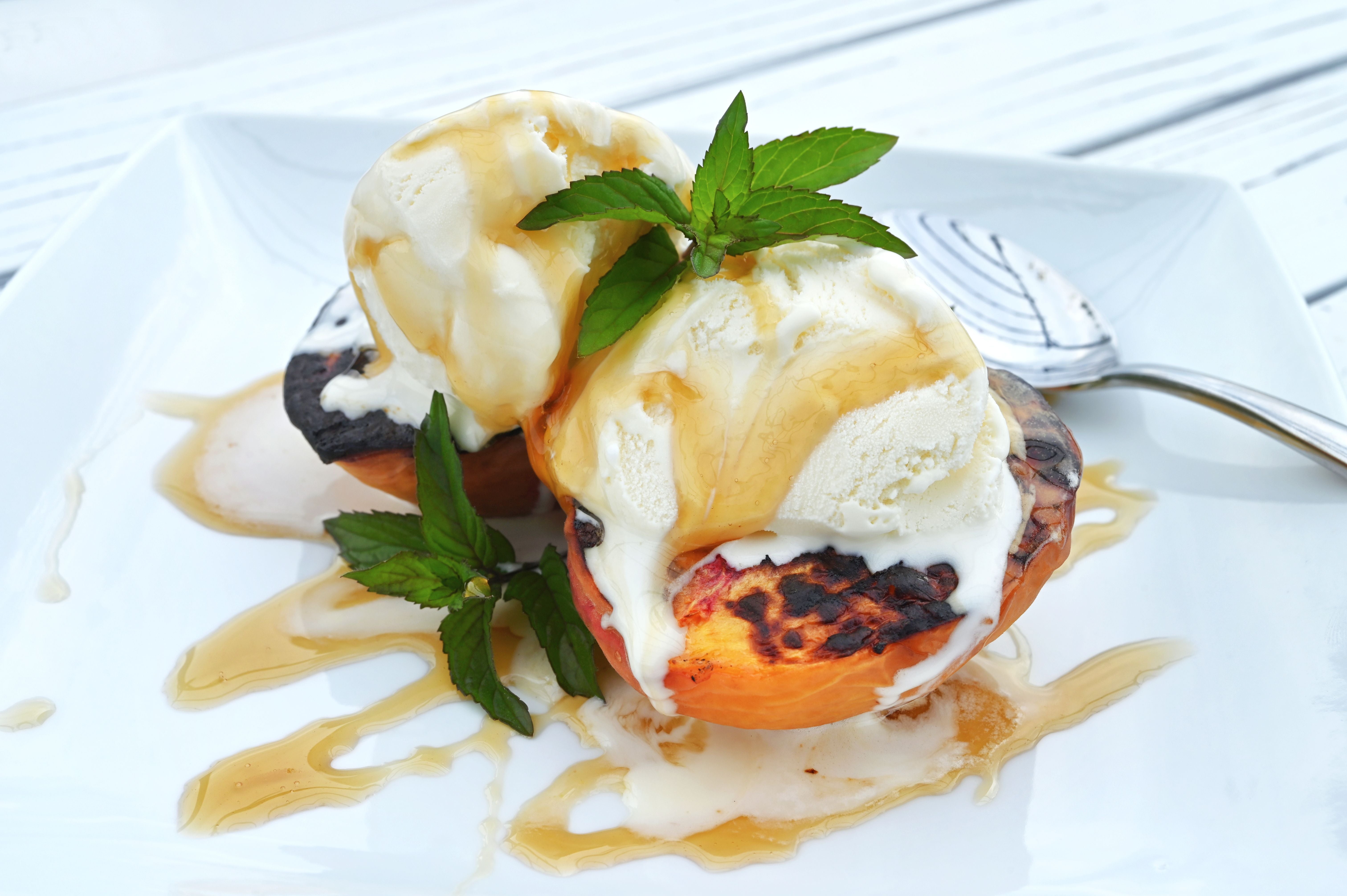 Gegrillte Pfirsiche mit Vanilleeis, Minzblatt und Karamellsauce auf einem weißen Teller.