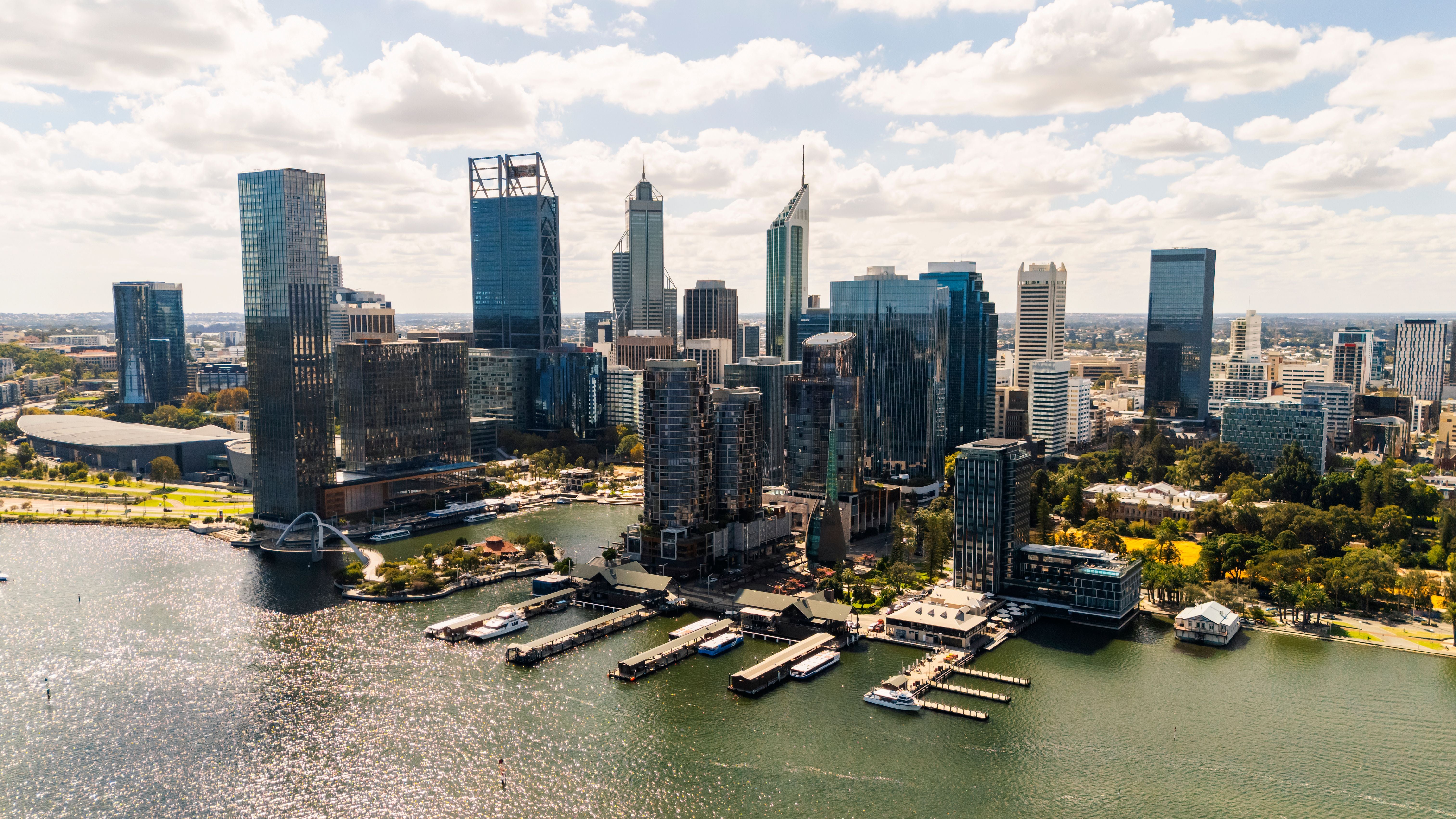 Luftaufnahme der Skyline von Perth mit modernen Hochhäusern am Wasser unter wolkigem Himmel.