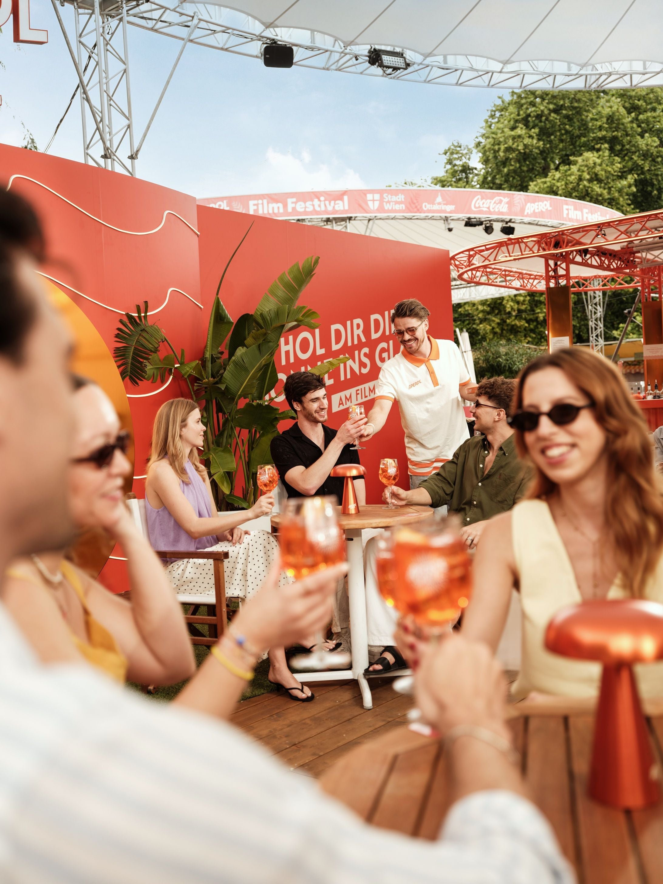 Menschen genießen Getränke an Tischen bei einem Sommer-Event auf einem Filmfestival.