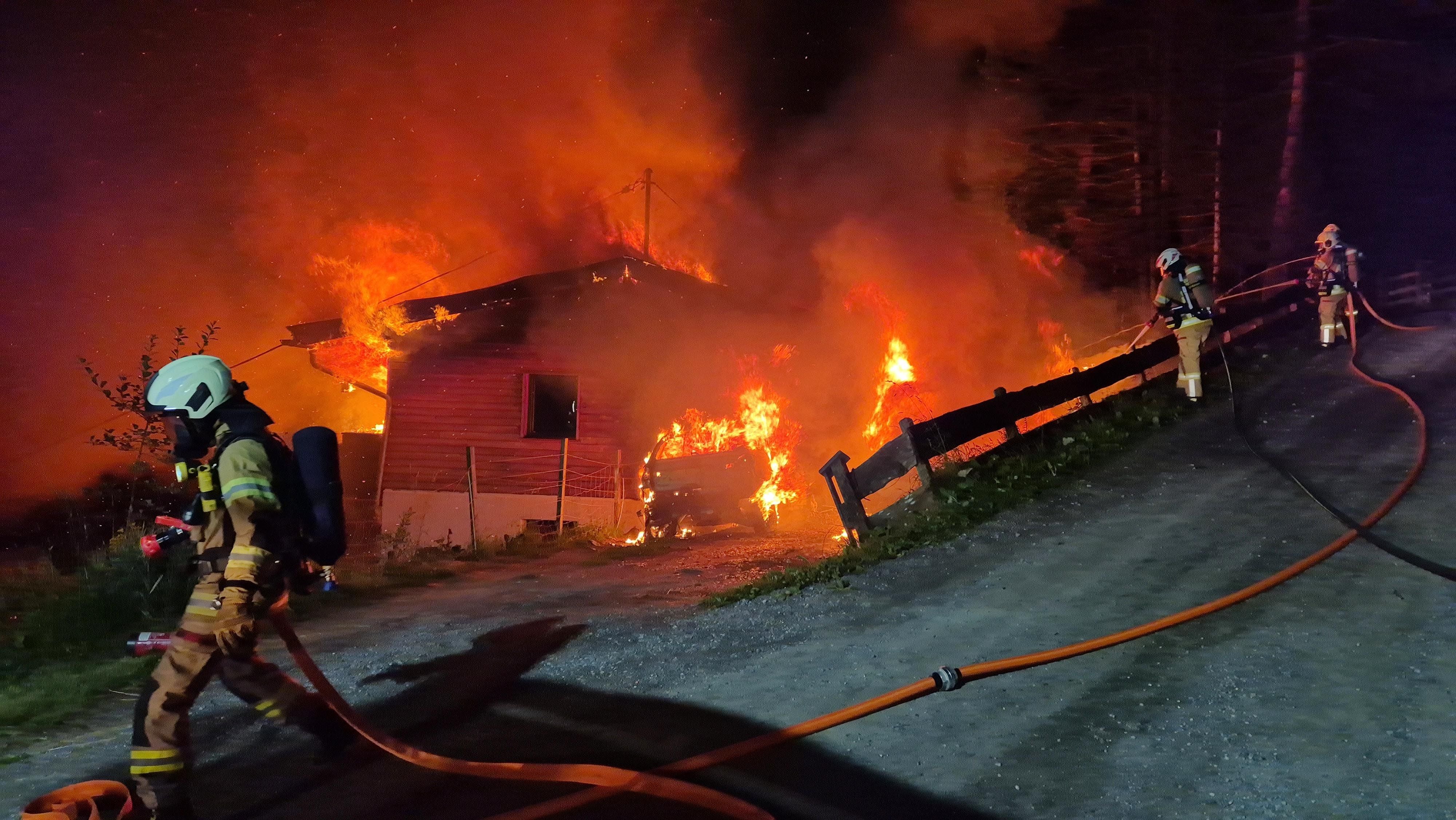 Feuerwehrleute bekämpfen nachts einen Großbrand in einem brennenden Holzhaus.