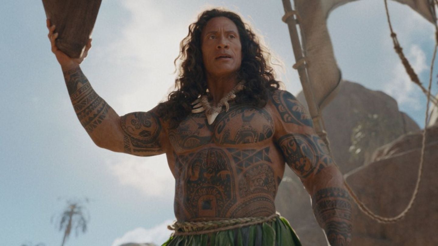 Mann mit langen Haaren und polynesischen Tattoos steht auf einem Boot unter freiem Himmel.
