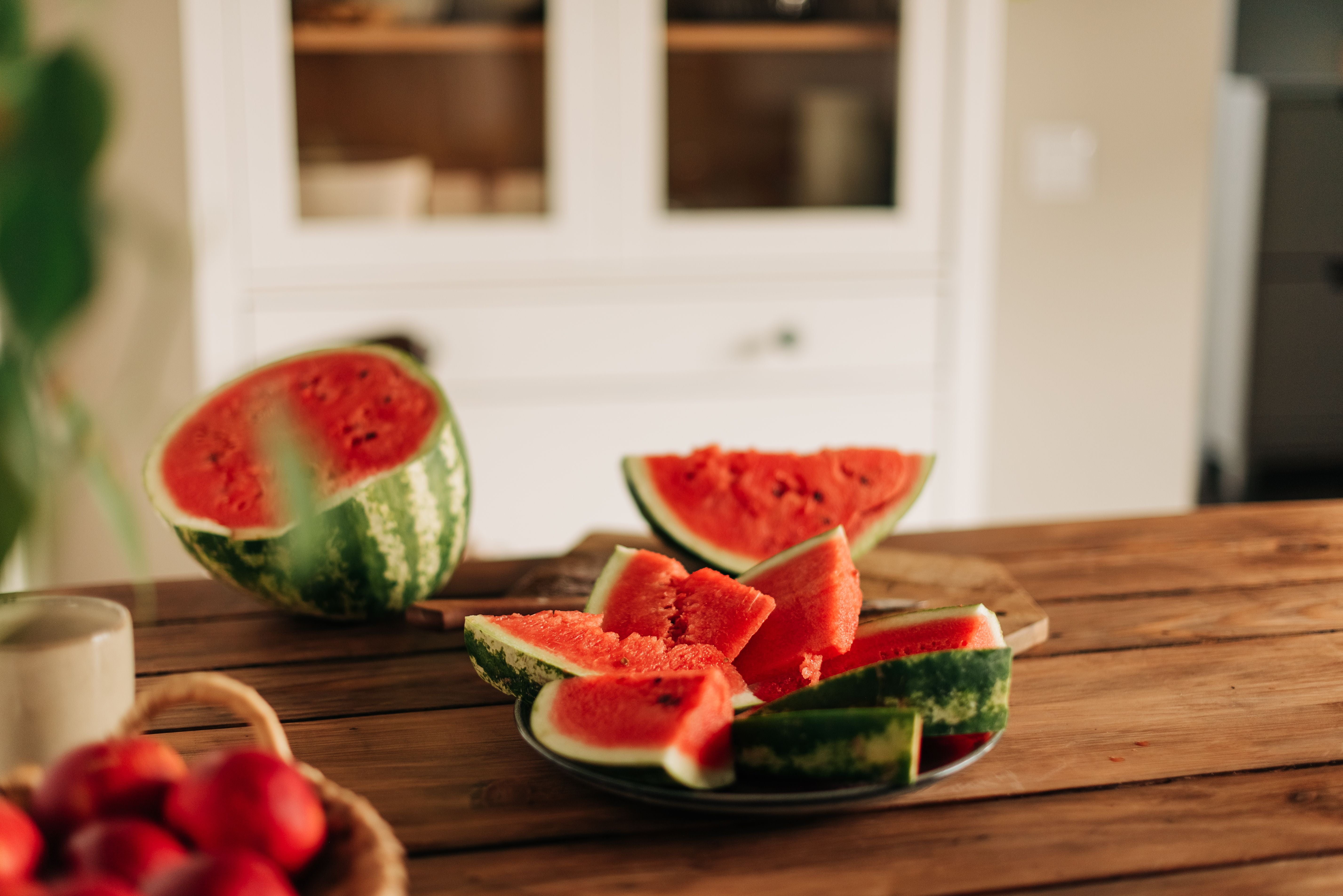 Geschnittene Wassermelone auf einem Holztisch in einer Küche, daneben ein Korb mit Pfirsichen.