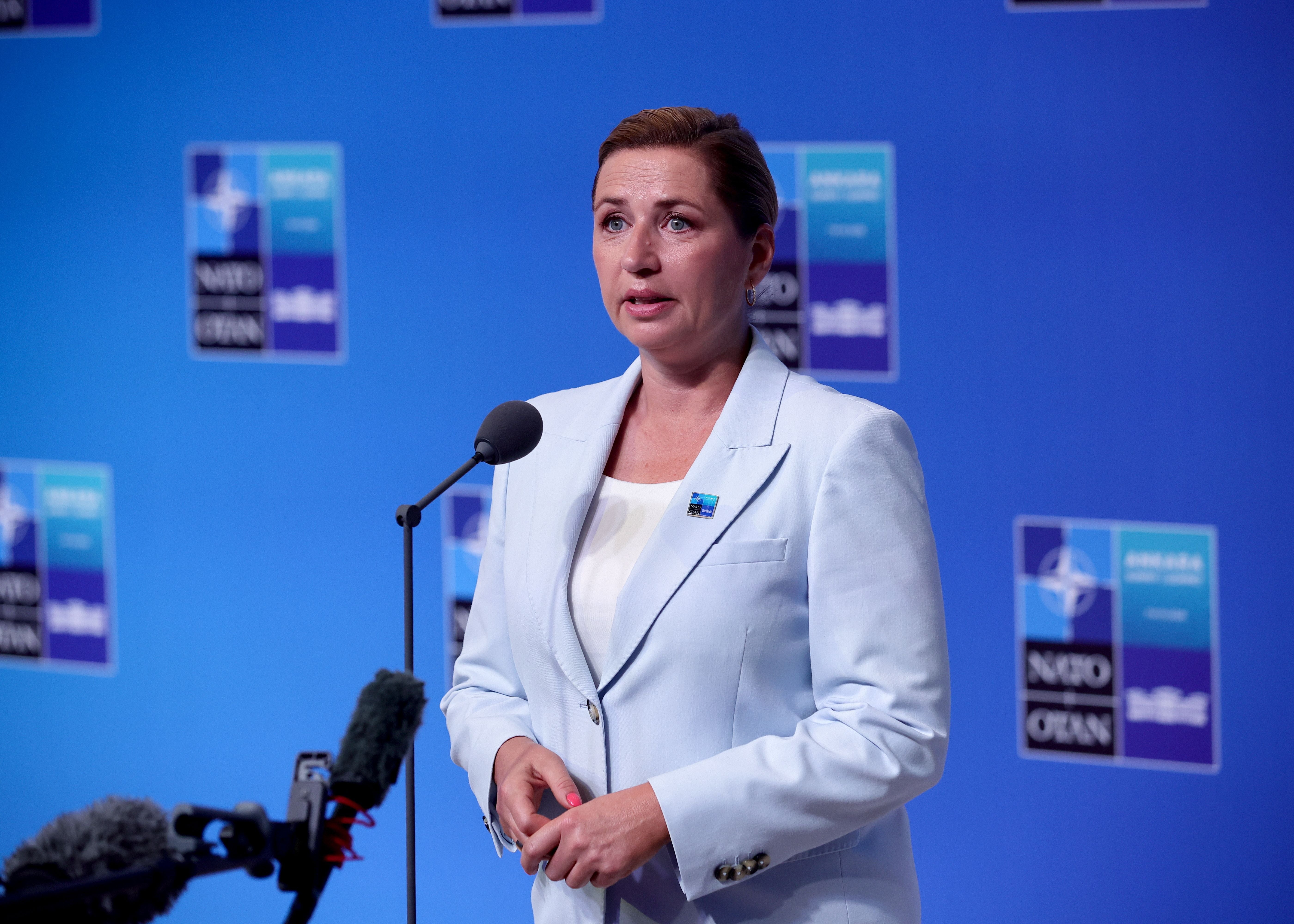 Eine Frau im hellblauen Blazer spricht auf einer NATO-Pressekonferenz vor Mikrofonen.