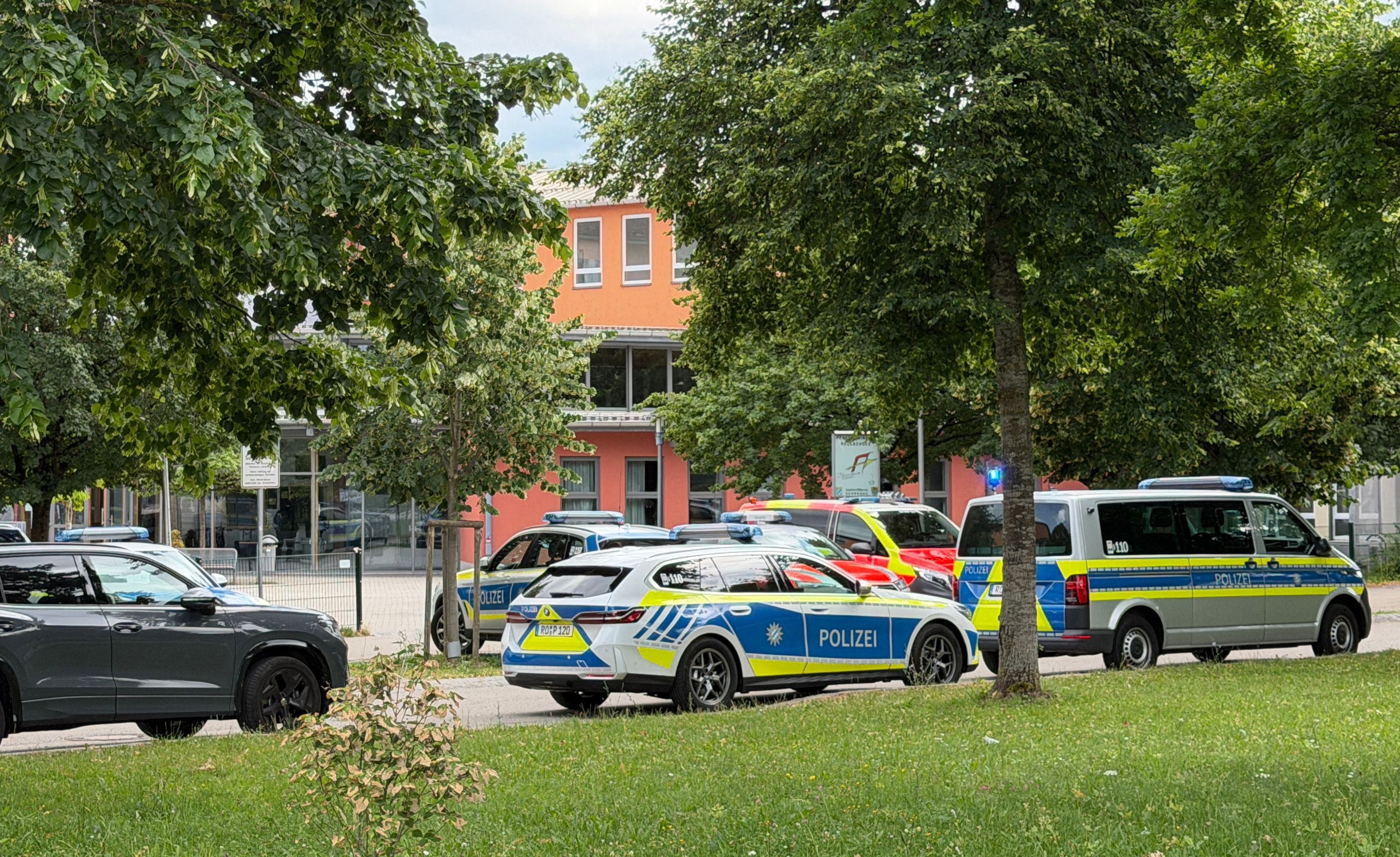 Mehrere Polizeiwagen stehen vor einer Schule in einer grünen, baumbestandenen Umgebung.