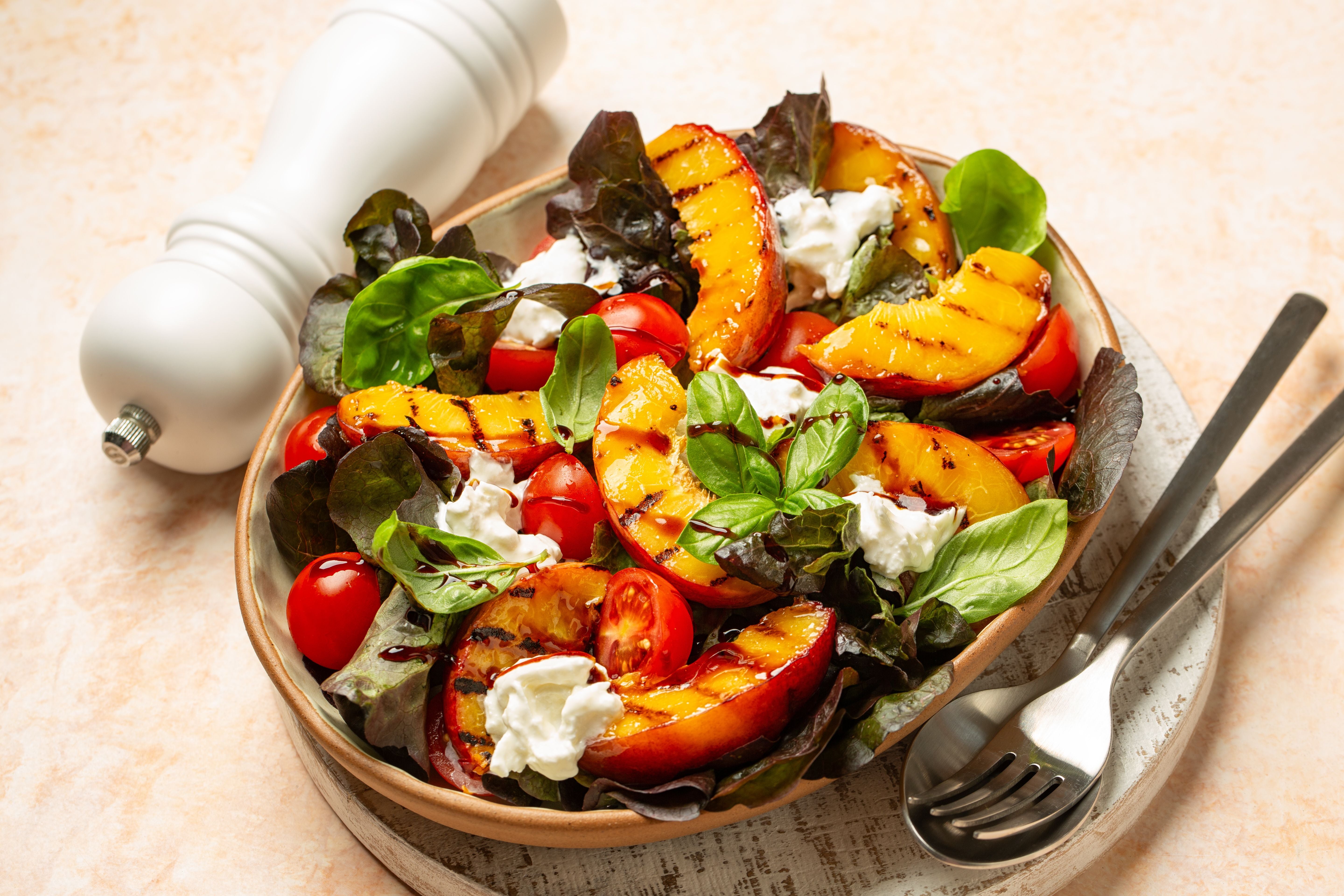 Salat mit gegrillten Pfirsichen, Tomaten, Basilikum und Burrata in einer Schale.