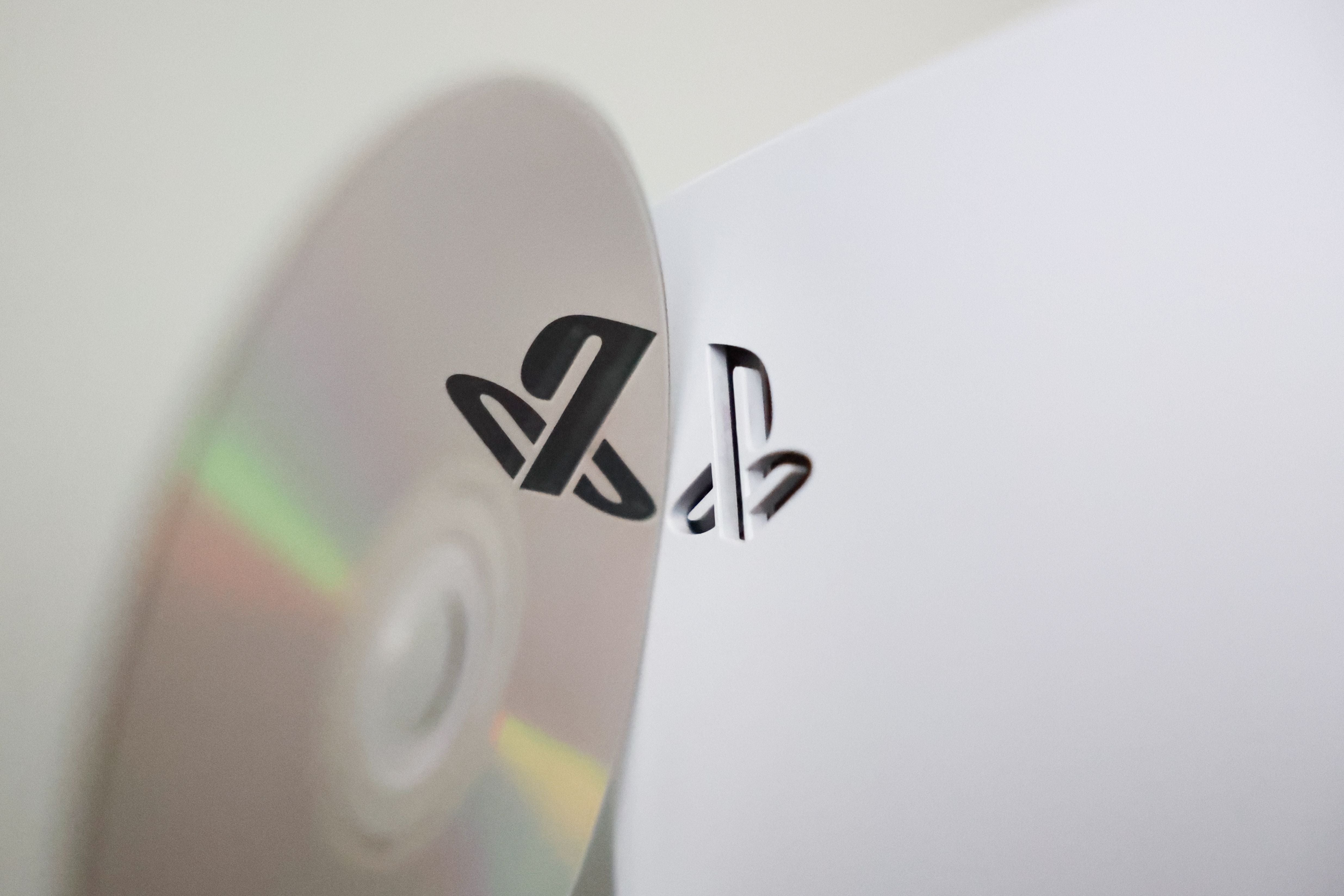 PlayStation-Logo auf einer Disc und einer weißen PlayStation 5 Konsole in Nahaufnahme.
