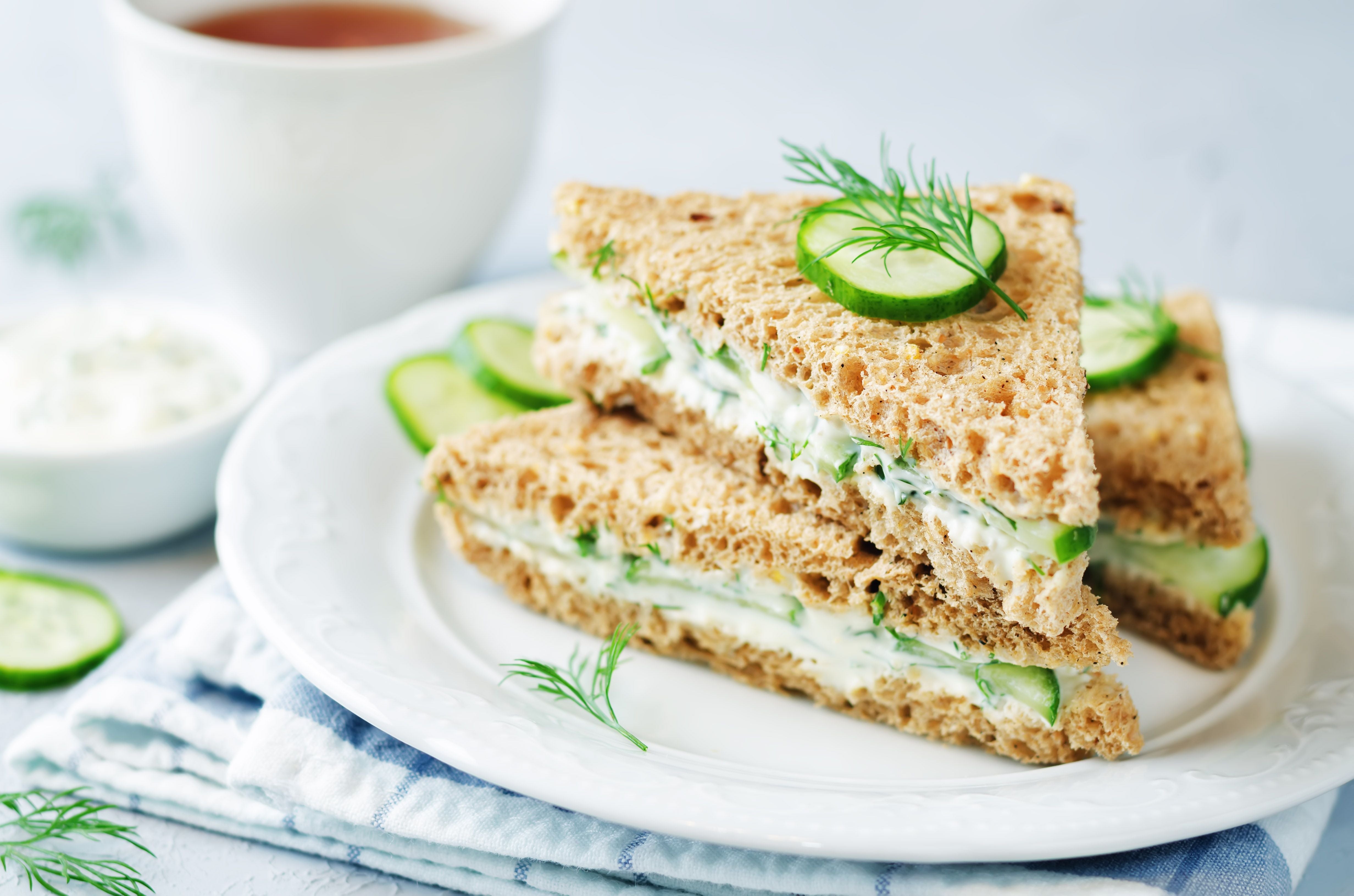 Zwei Dreieck-Sandwiches mit Frischkäse, Gurke und Dill auf einem weißen Teller.