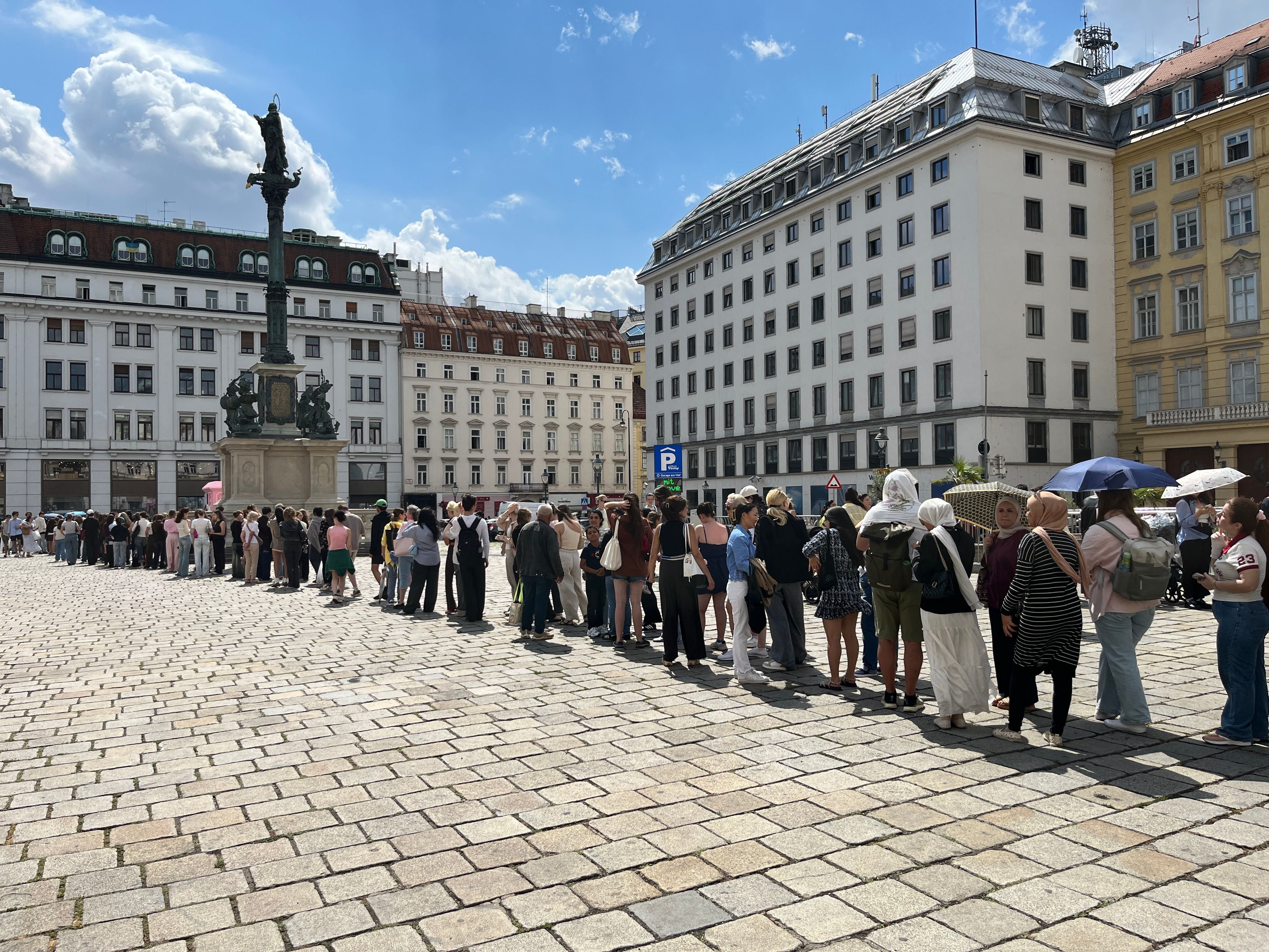 Viele Menschen stehen bei Sonnenschein vor einem Dior Pop-up auf einem historischen Platz Schlange.