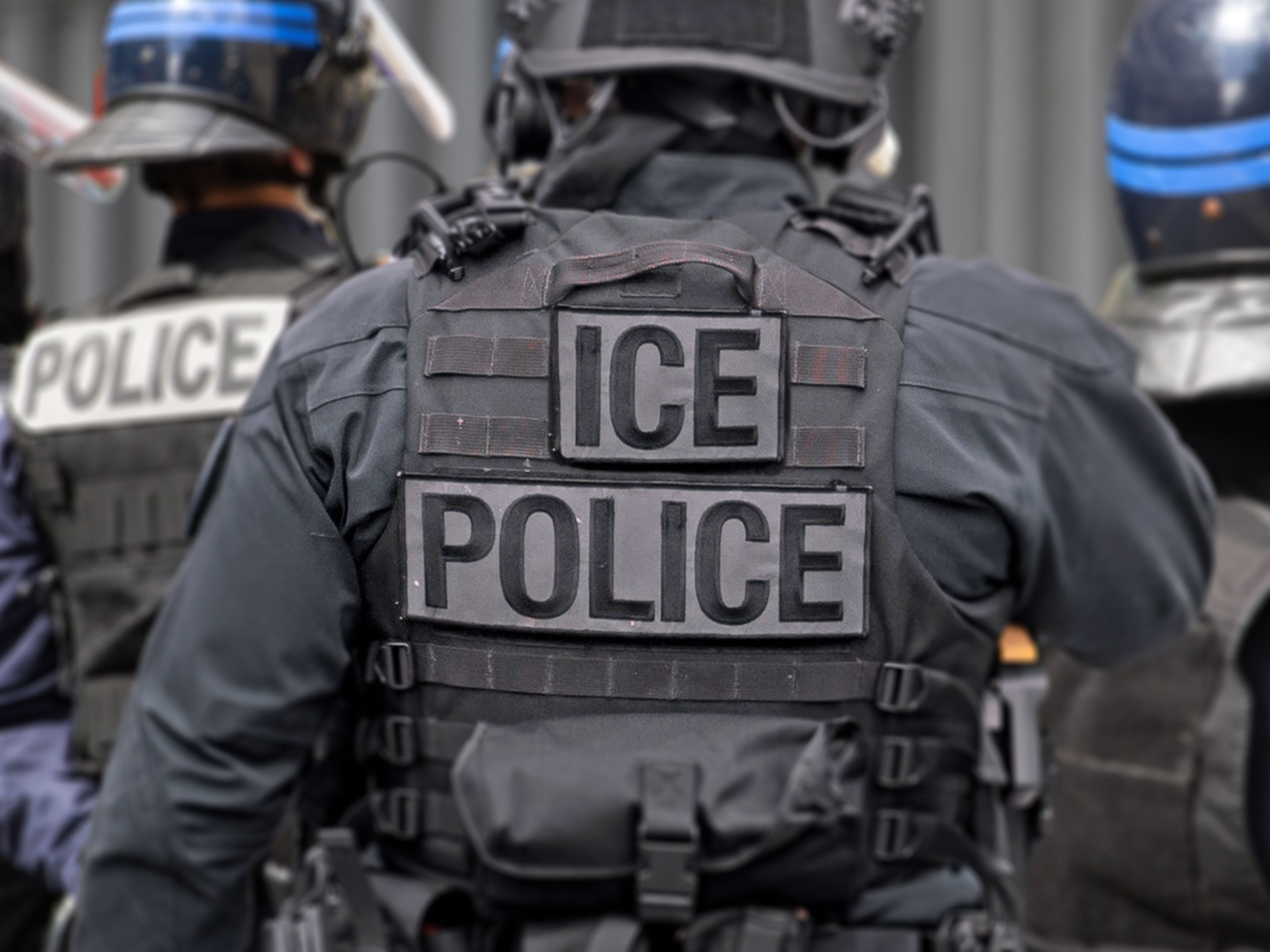 Mehrere Polizisten in Schutzkleidung mit „ICE POLICE“-Aufschrift auf der Rückseite der Weste.