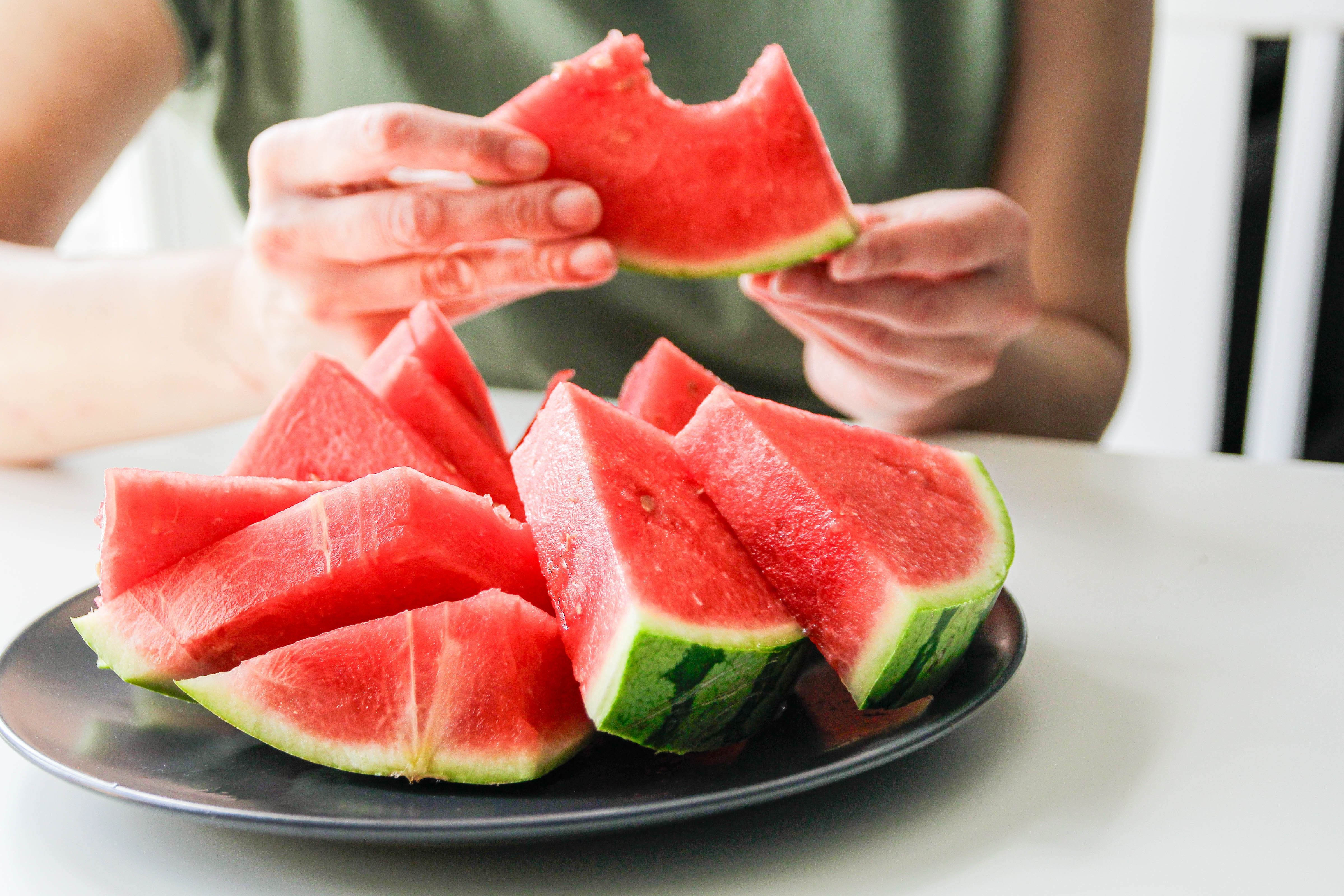 Person hält ein Stück Wassermelone mit Biss, vor einem Teller mit weiteren Stücken.
