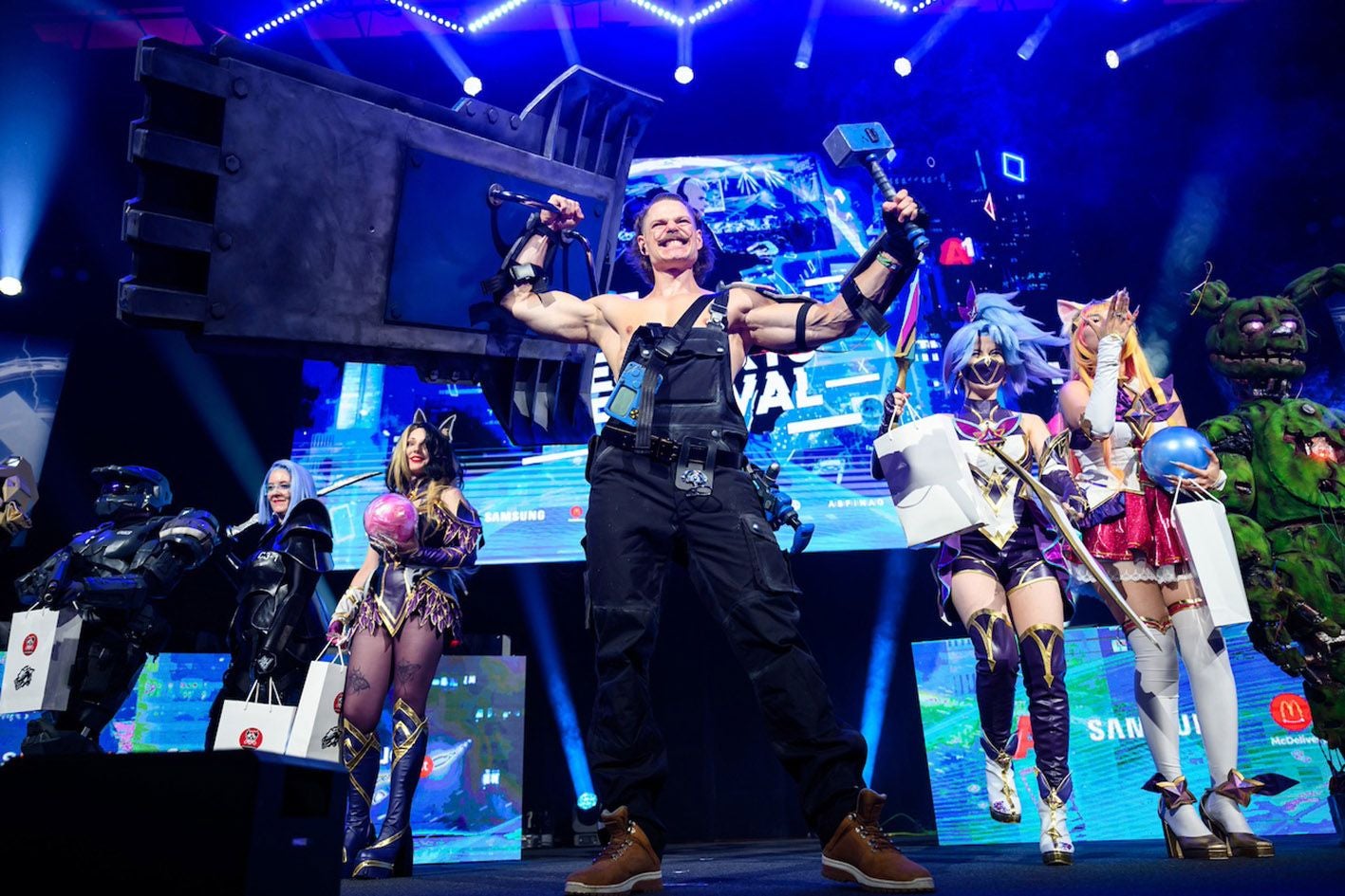 Menschen in aufwendigen Cosplay-Kostümen stehen jubelnd auf einer Bühne beim Esportsfestival.
