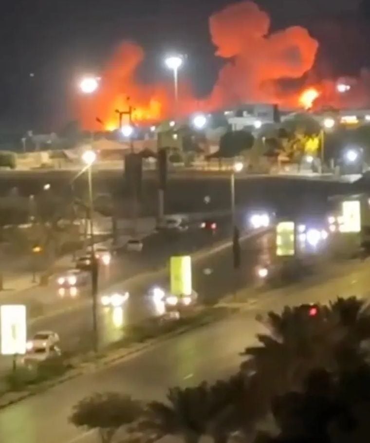 Große Explosion mit Feuerschein bei Nacht in einer Stadt, Autos auf beleuchteter Straße im Vordergrund.