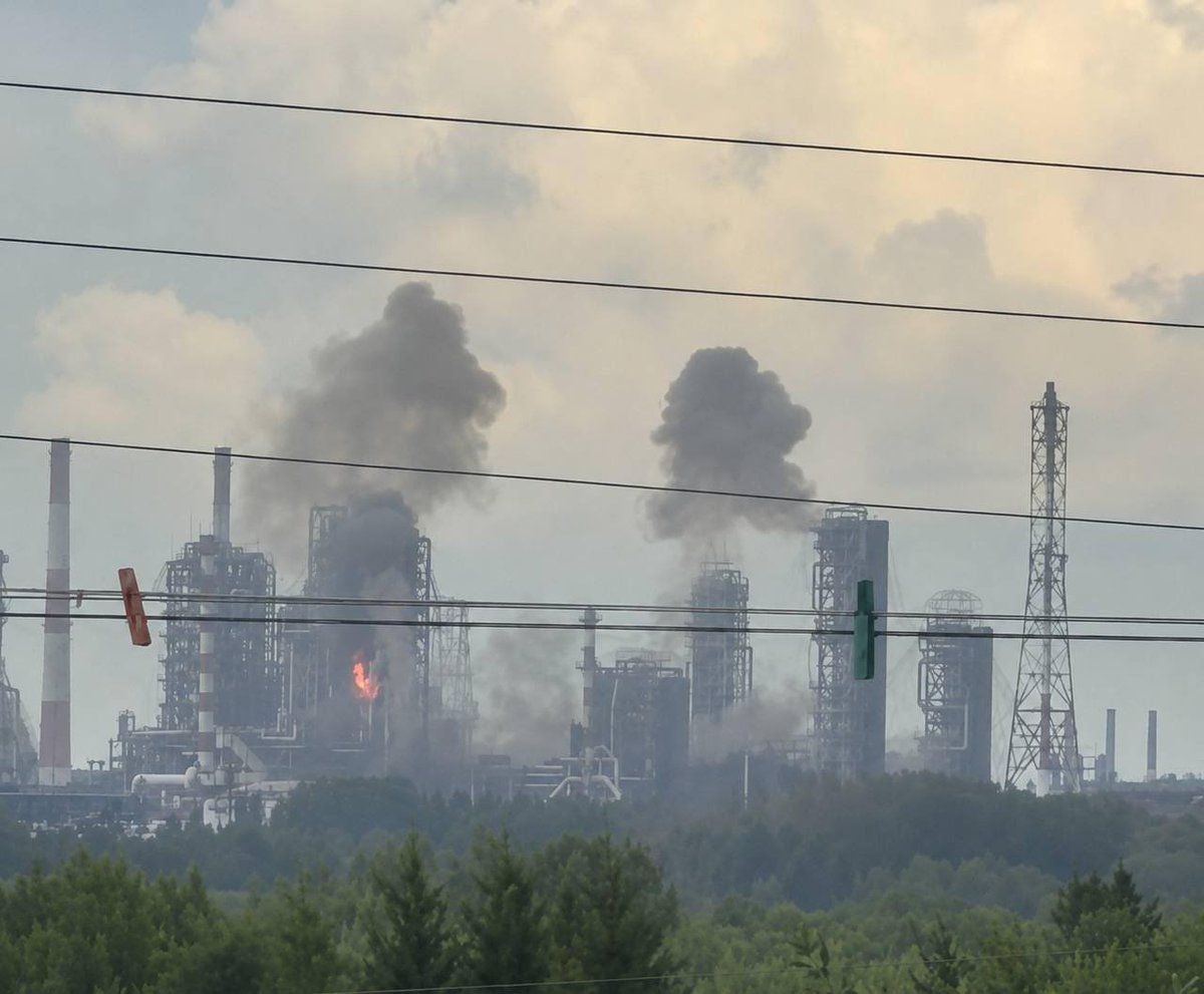 Rauch steigt über einer brennenden Industrieanlage in Omsk auf, umgeben von grünen Bäumen.