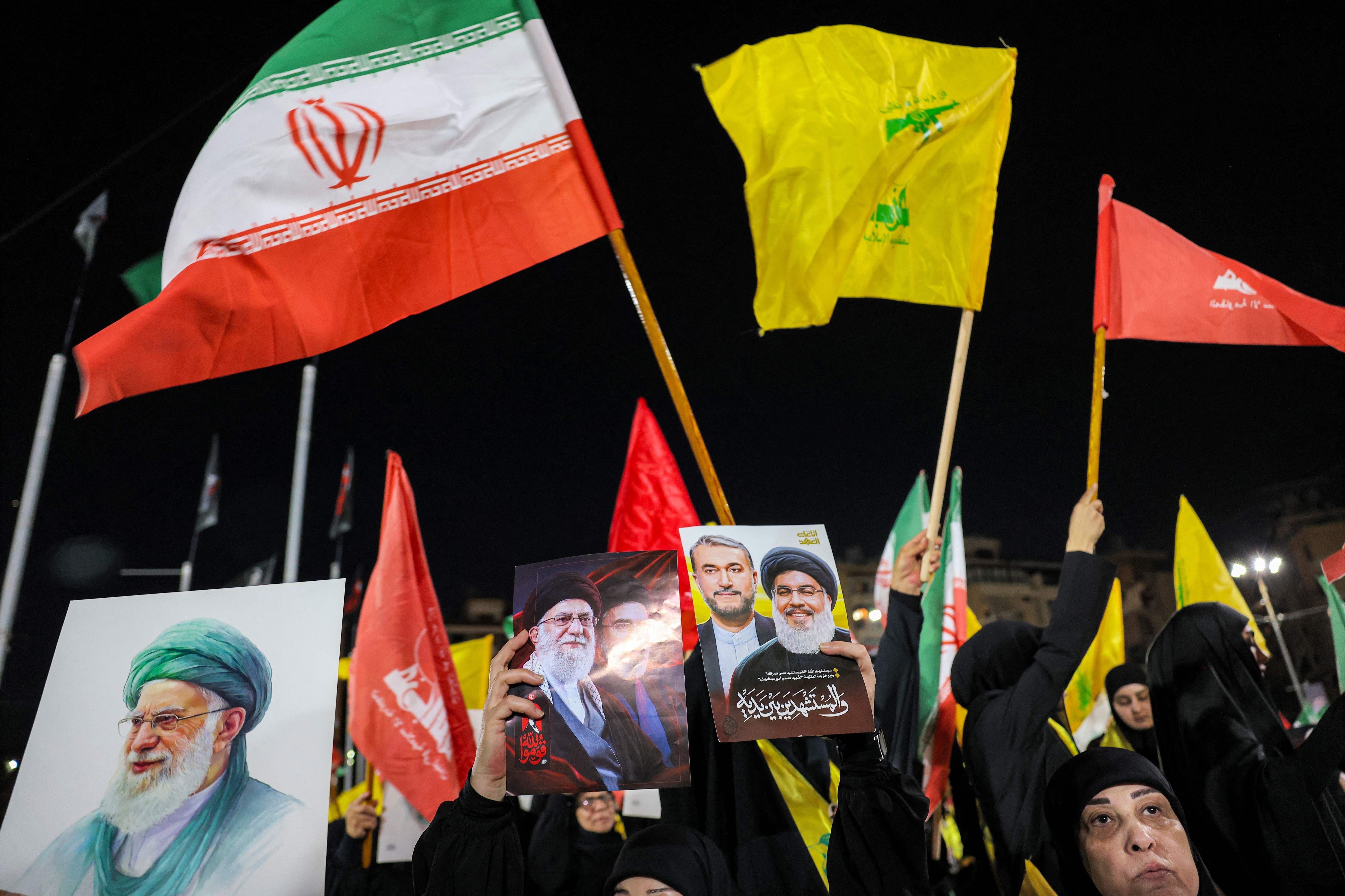 Frauen halten Bilder und Fahnen bei einer Gedenkveranstaltung mit iranischer und Hisbollah-Flagge.