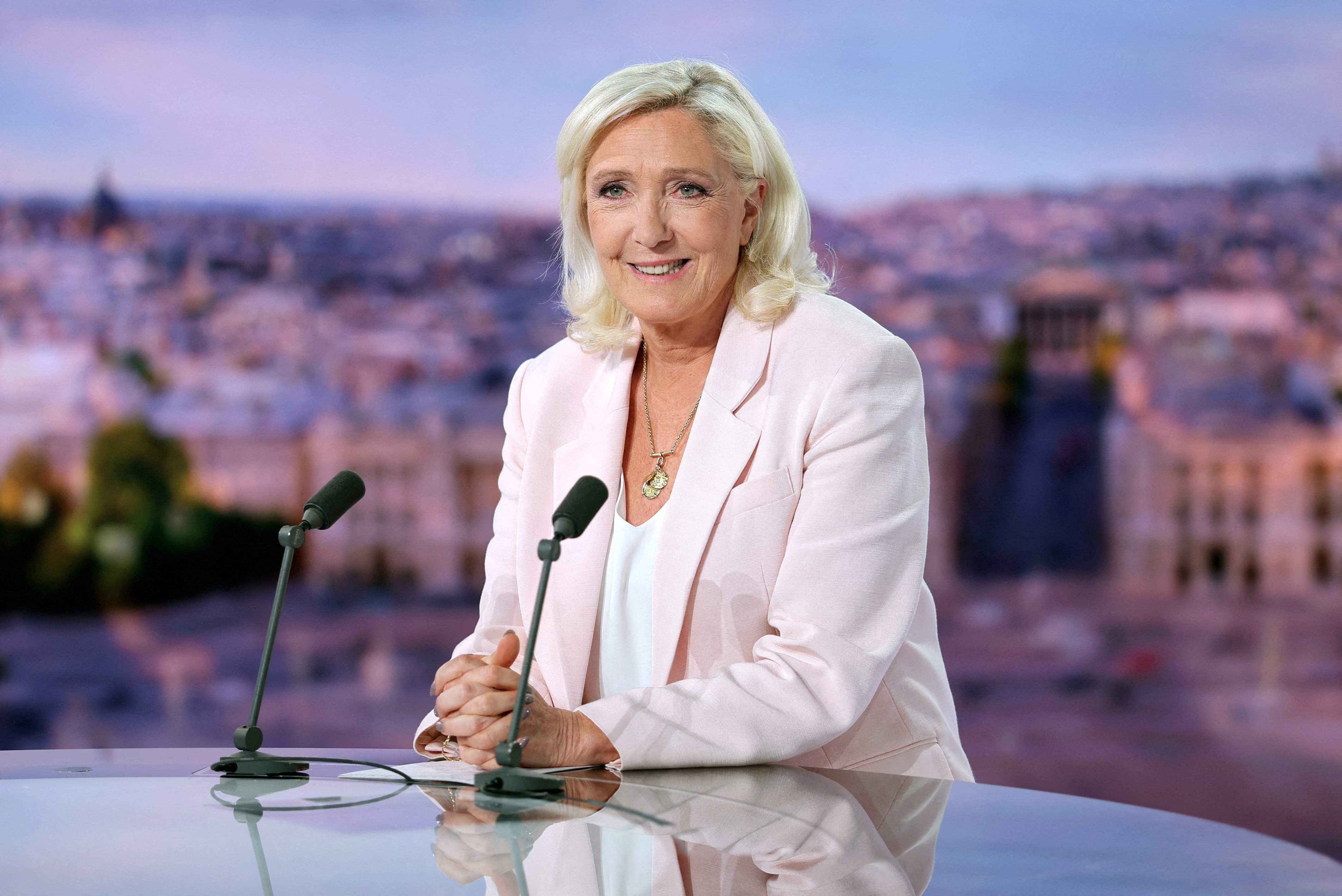Frau mit blondem Haar im hellen Blazer sitzt lächelnd bei einem Interview vor zwei Mikrofonen.