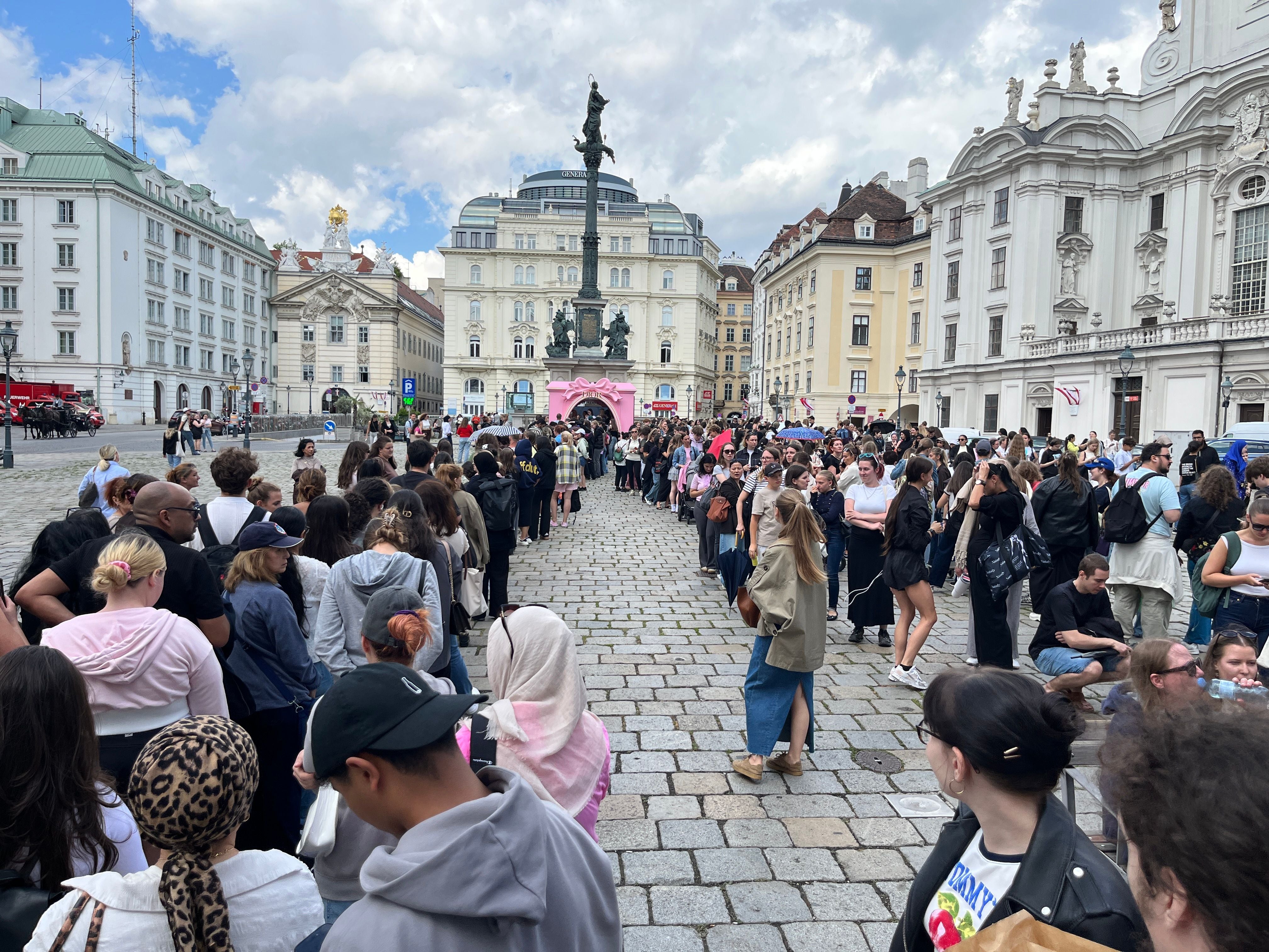 Viele Menschen stehen vor einem Dior Pop-up in einer historischen Stadt in einer langen Schlange.