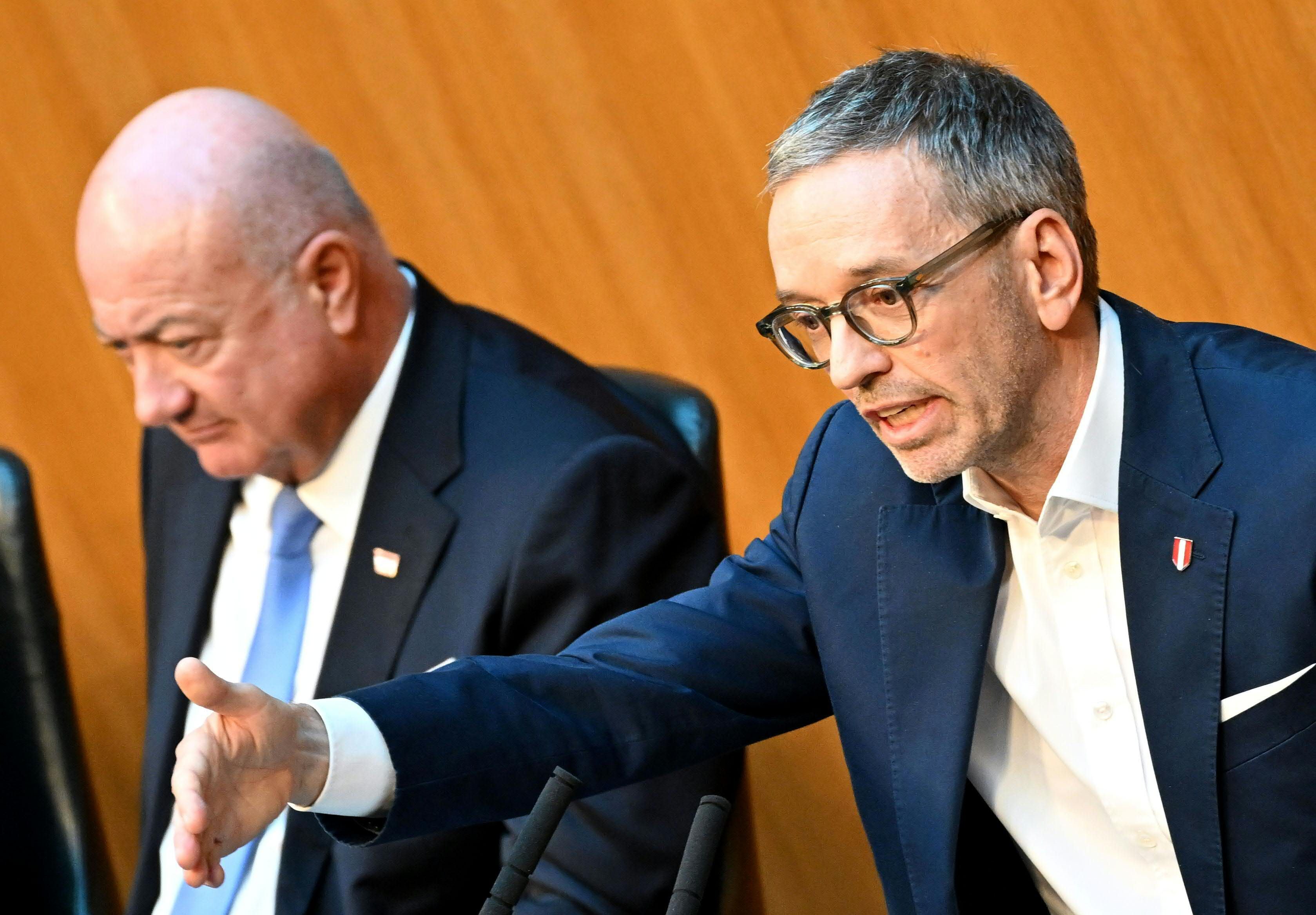 Zwei Männer im Anzug sprechen bei einer Parlamentssitzung in Wien.