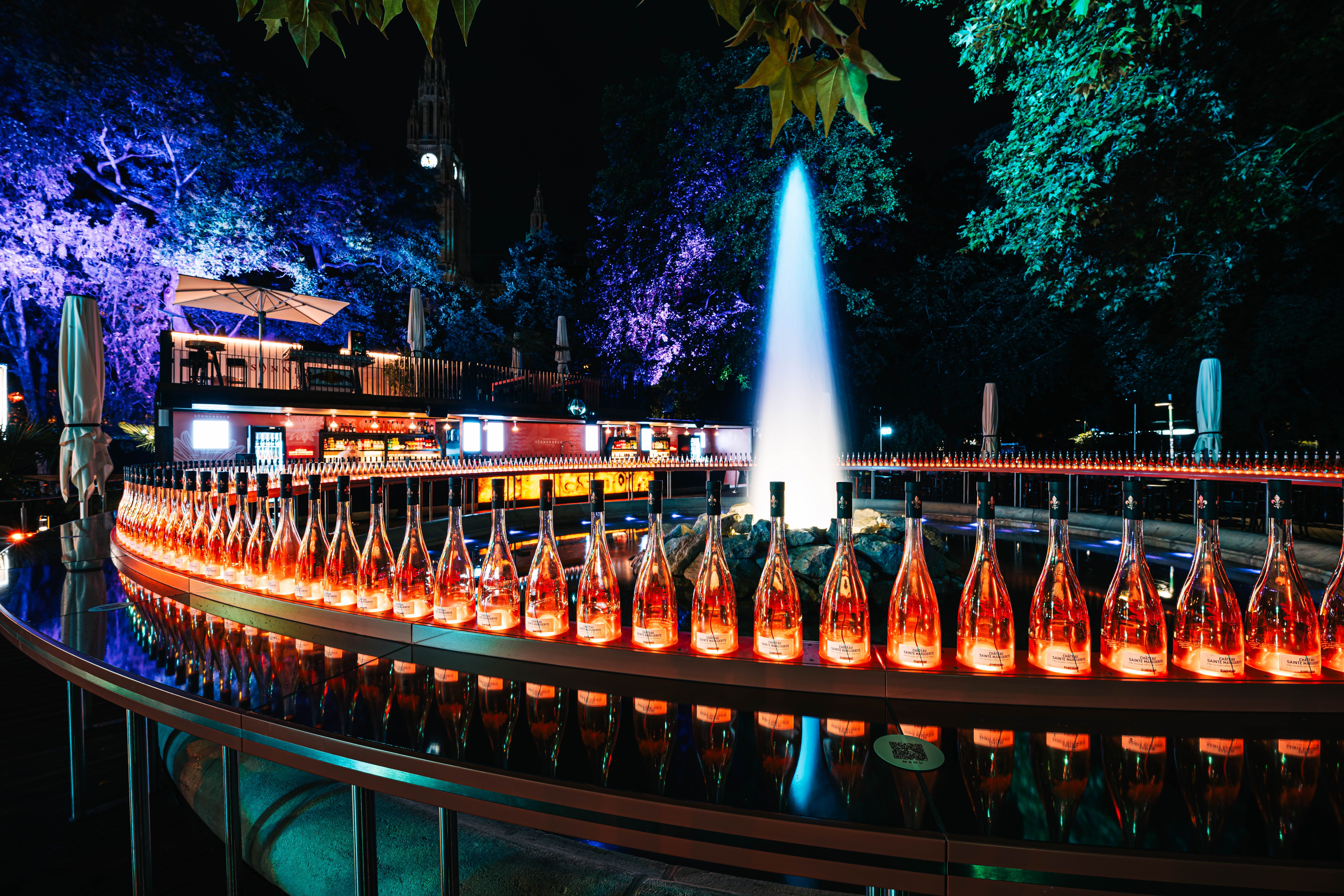 Beleuchtete Weinflaschen und ein Springbrunnen bei Nacht auf einem Filmfestival.