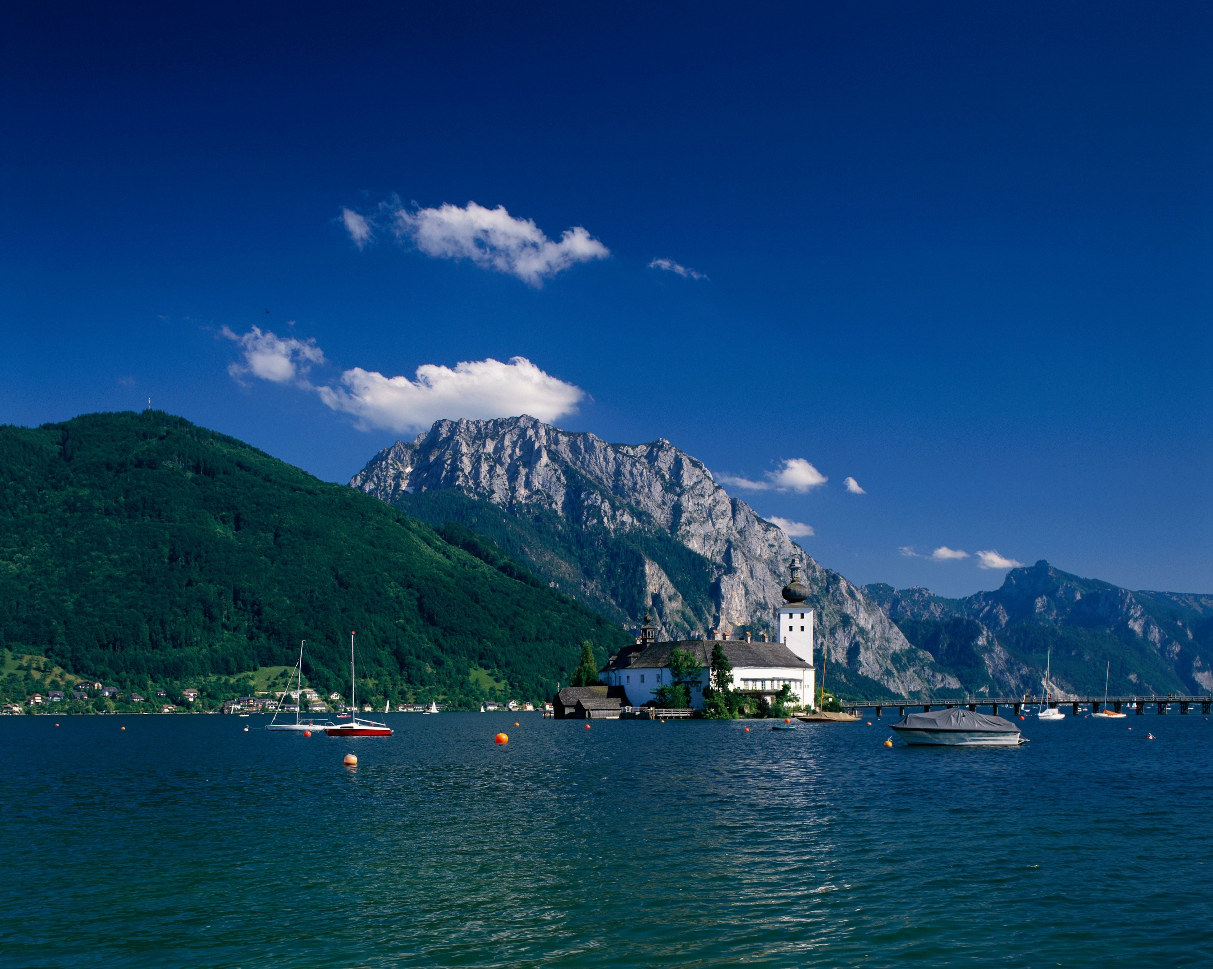 See mit Segelbooten, einer Inselkirche und Bergen im Hintergrund unter klarem, blauem Himmel.