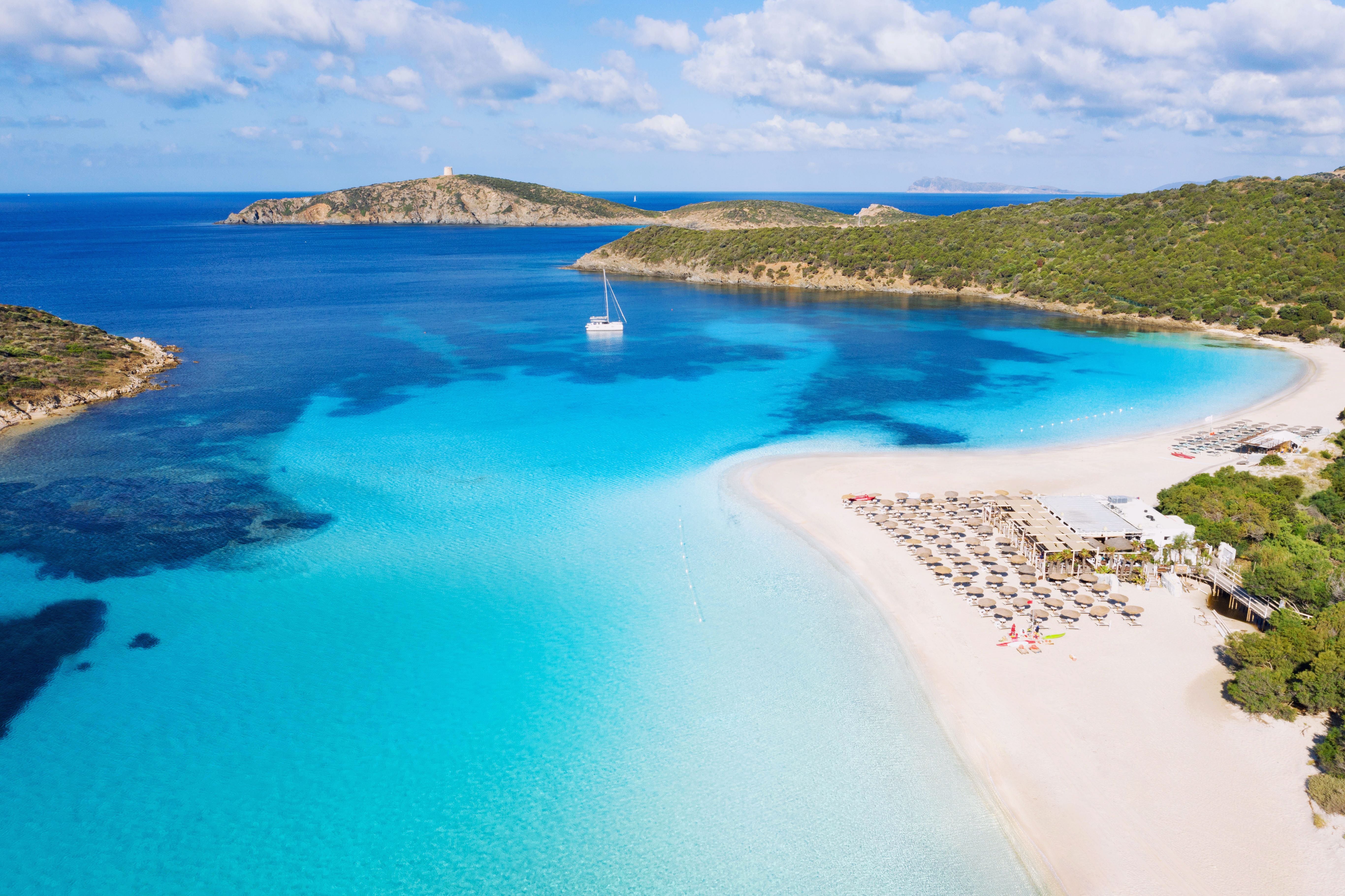 Luftaufnahme vom Strand Tueredda auf Sardinien mit türkisblauem Wasser und Liegestühlen.