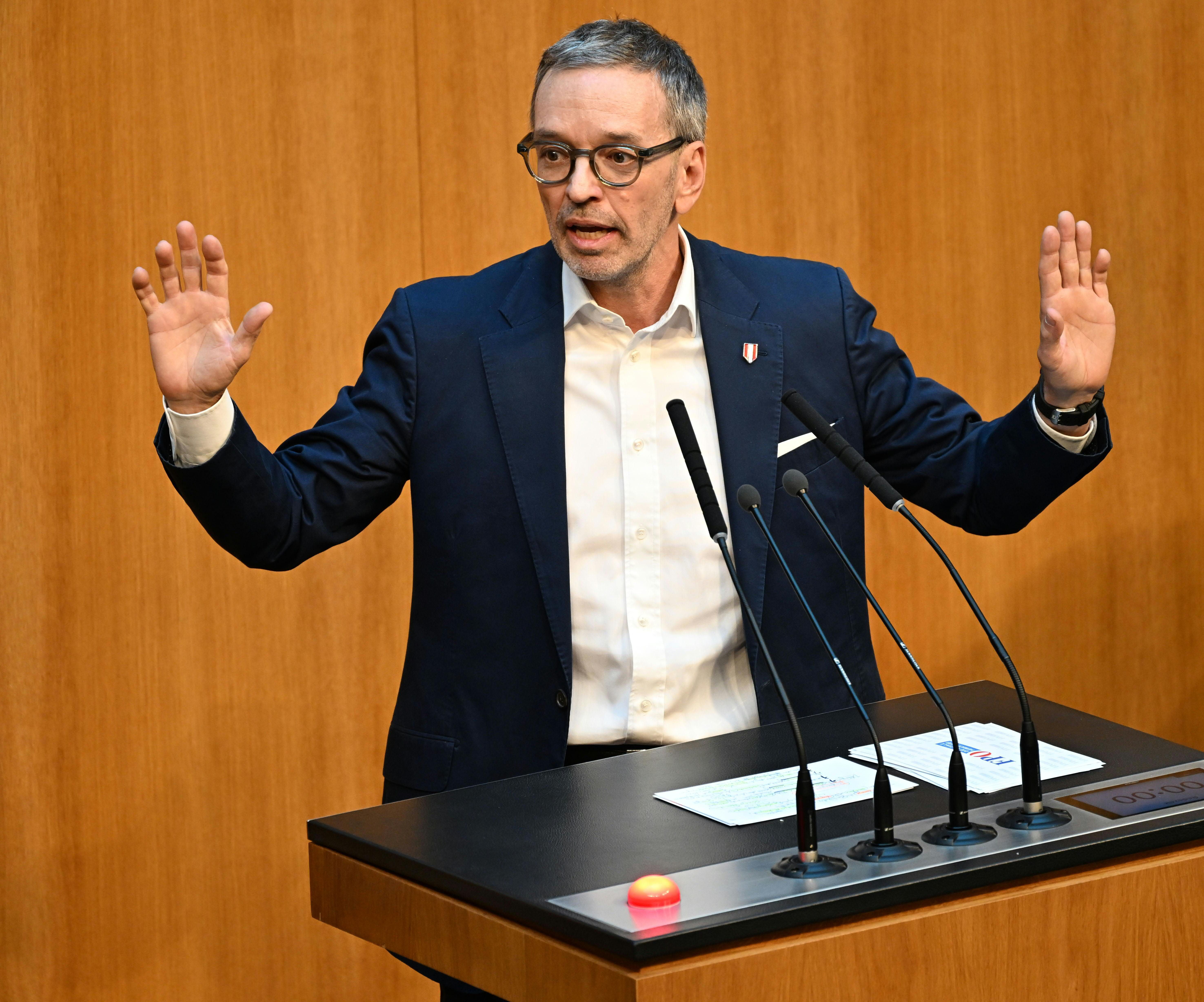 Ein Mann spricht gestikulierend an einem Rednerpult mit mehreren Mikrofonen im Parlament.