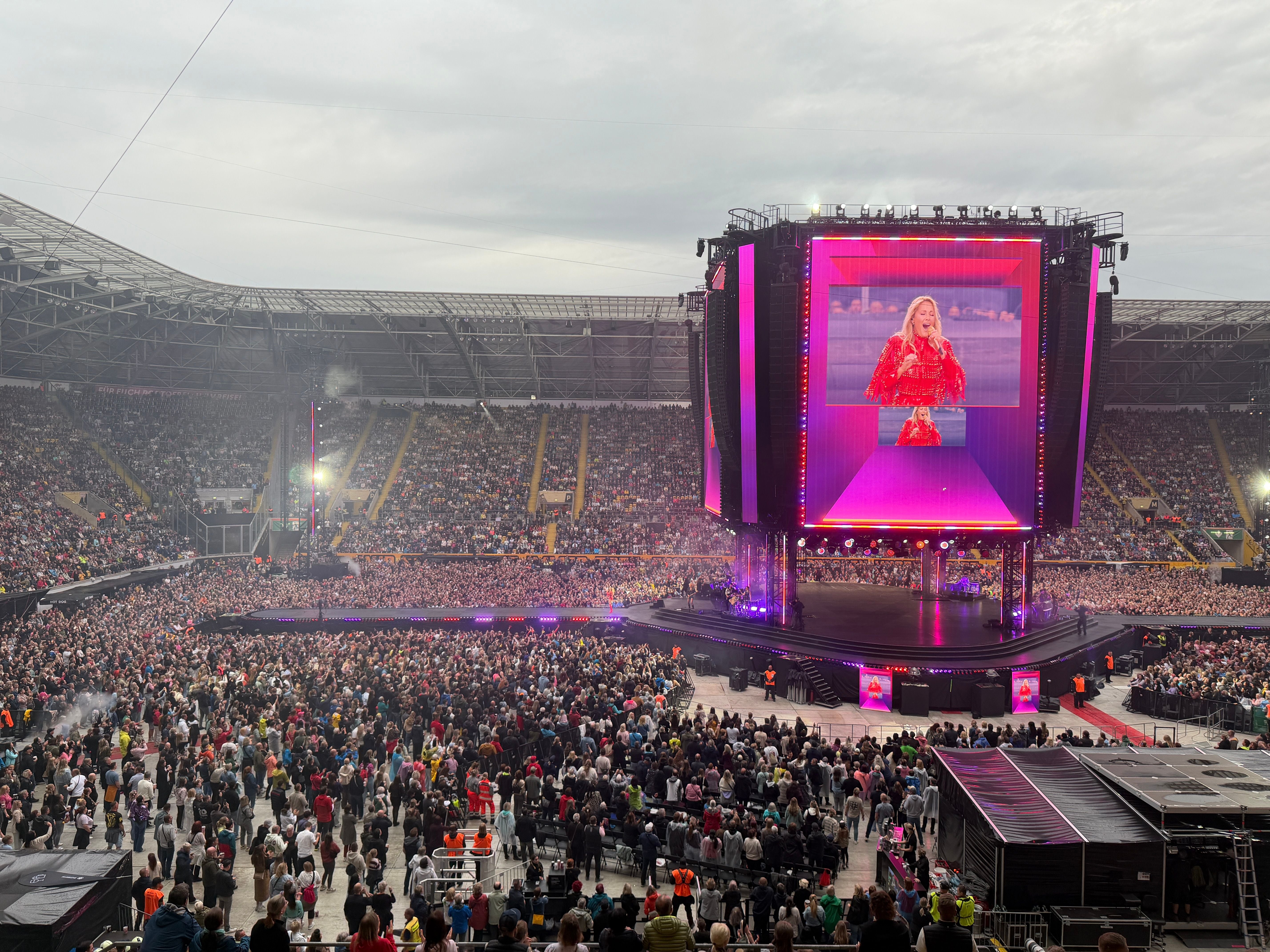 Großes Open-Air-Konzert in einem Stadion mit Bühne und großem Bildschirm, viele Zuschauer.